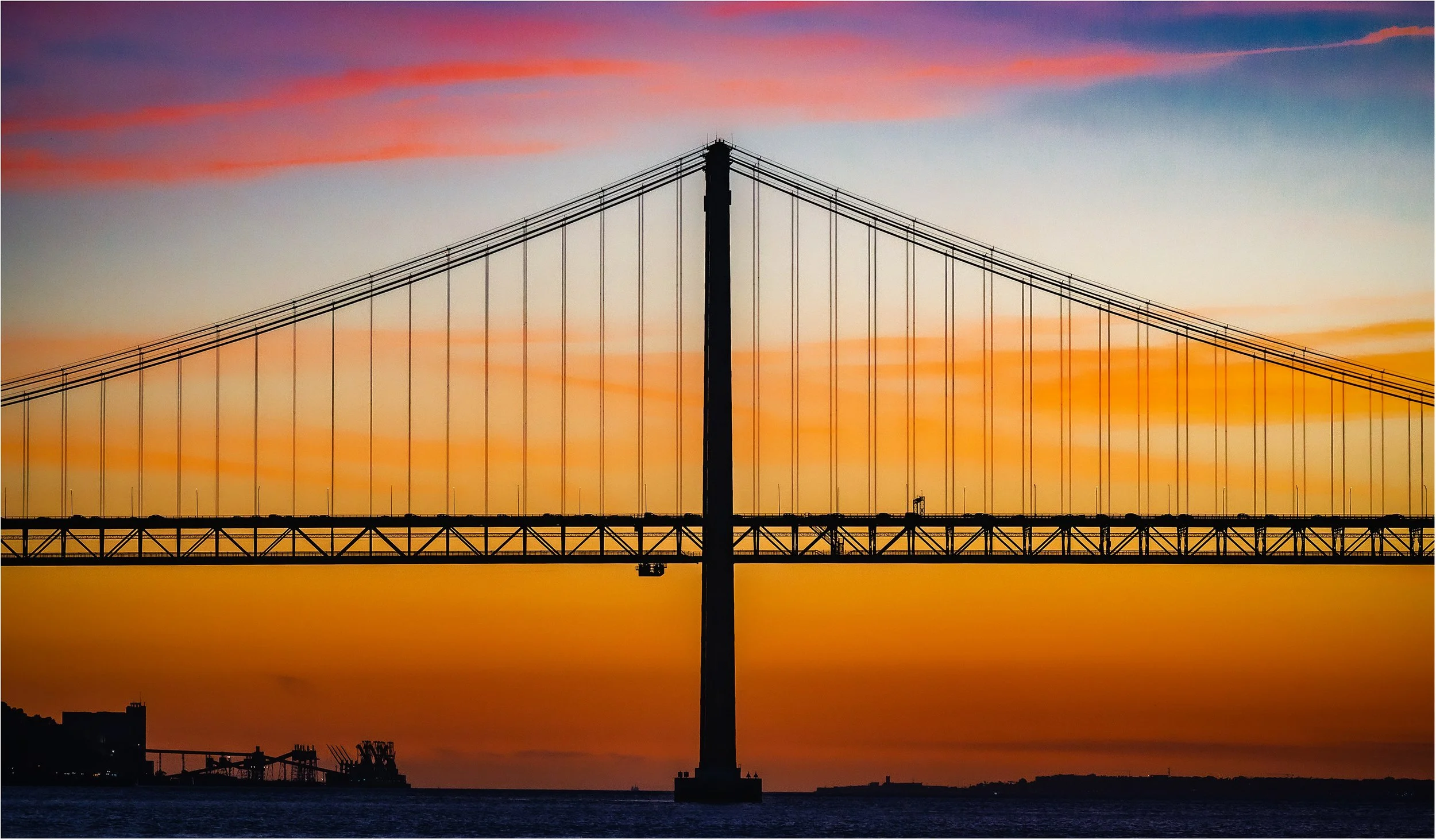 Die Brücke Ponte 25 de Avril in Lissabon bei Sonnenuntergang bietet fantastische Farben. Auf der obenen Ebene fahren die Autos (genau schauen, sie sind zu sehen), auf der unteren fahren Züge.