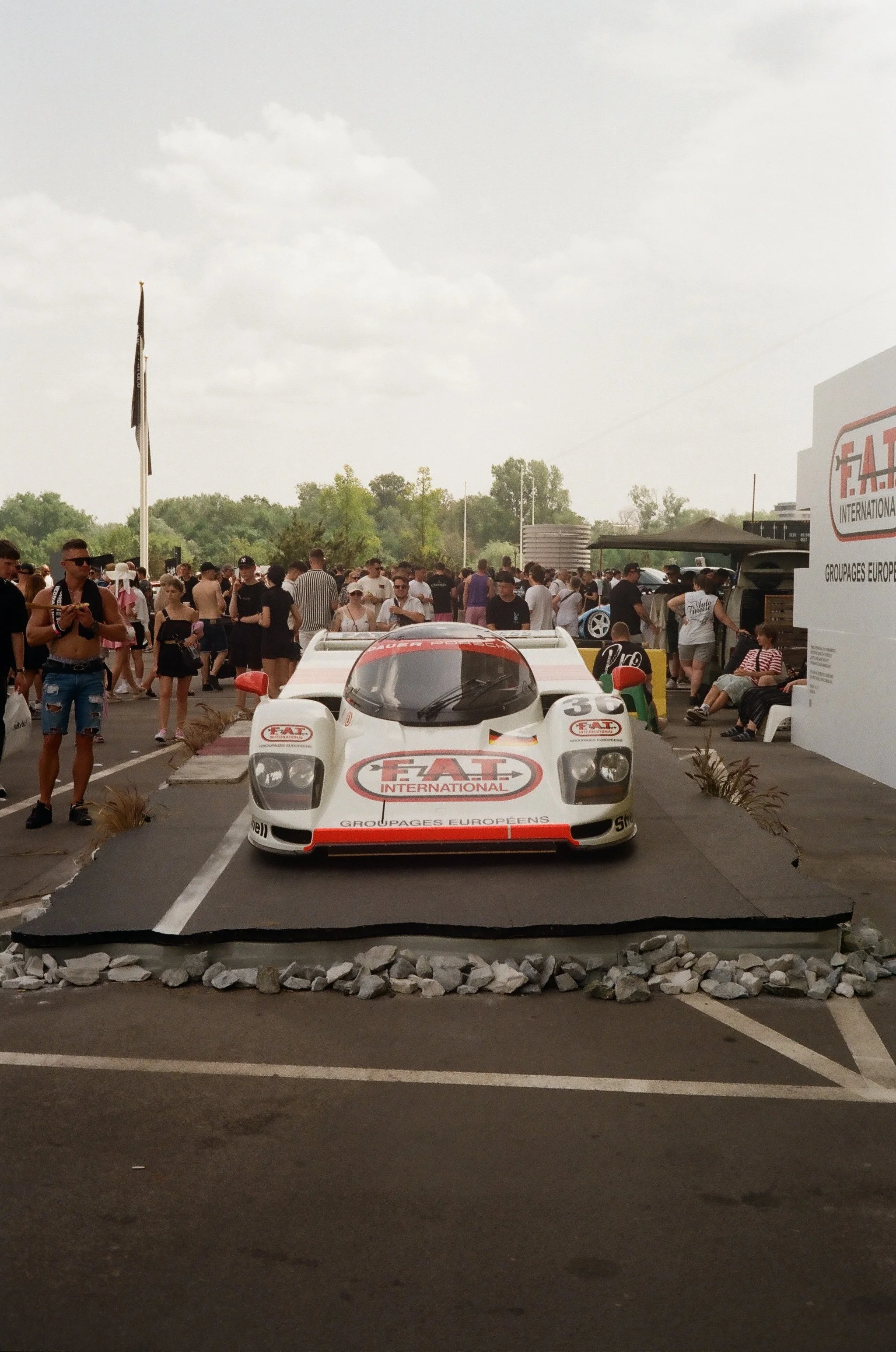 A vintage racing car with FIA and Group C logos displayed at a car event, surrounded by a crowd of people.