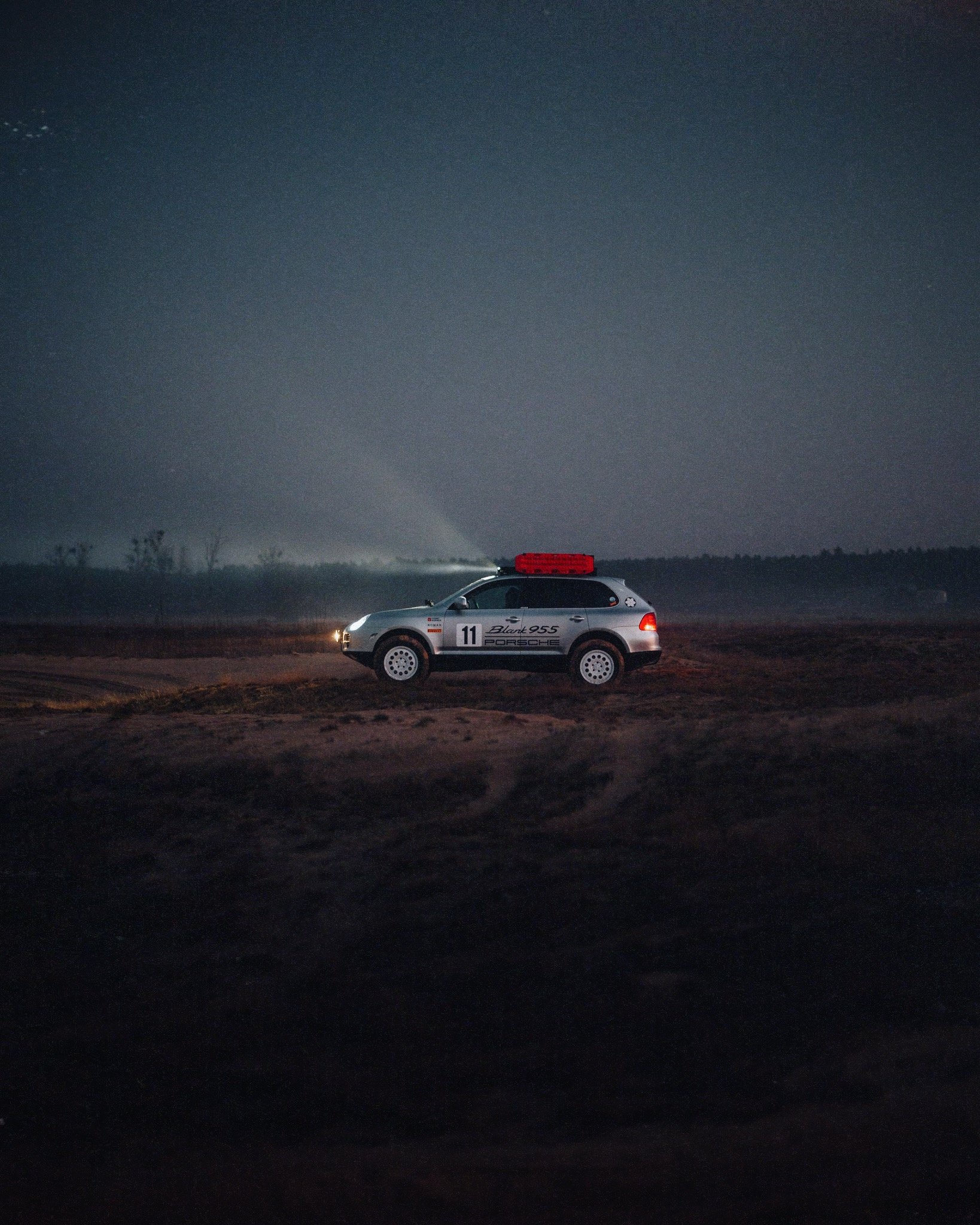 Nighttime image of a landscape with a racing car on rough terrain, under a dark sky with stars.