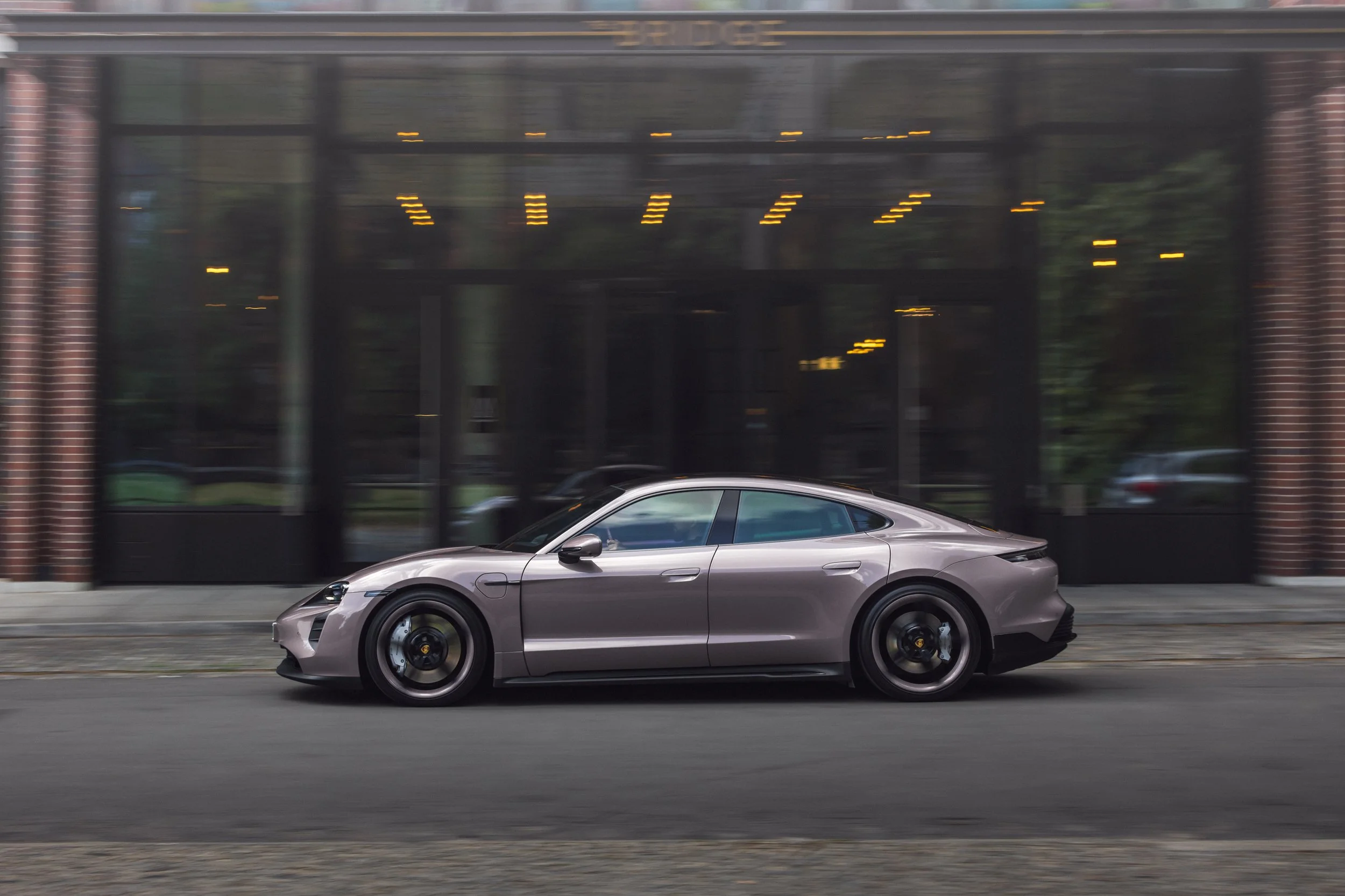 A silver Porsche sports car driving on city street in front of a modern glass building.