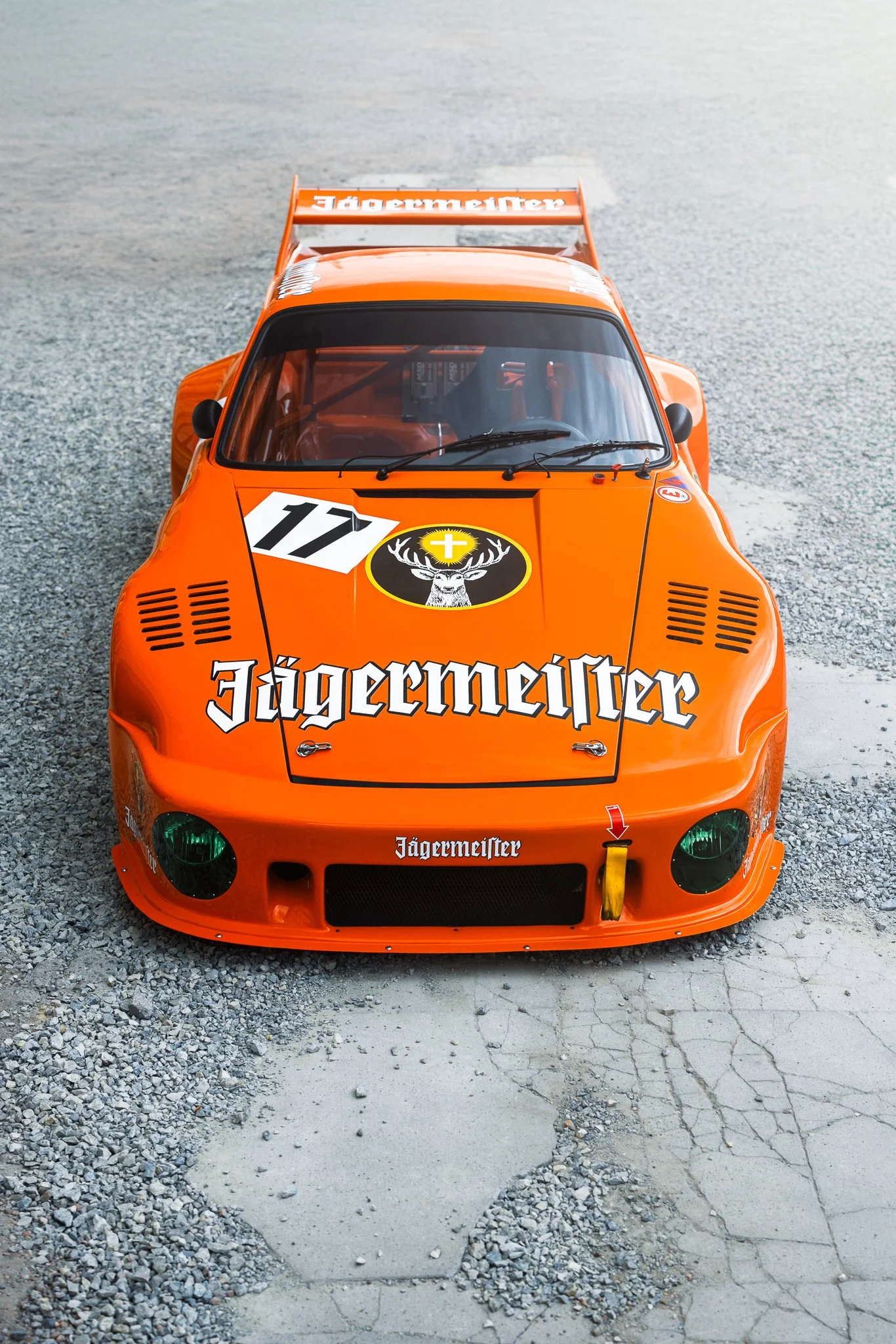 A vintage orange race car with Jägermeister branding, numbered 17, parked on a gravel surface.