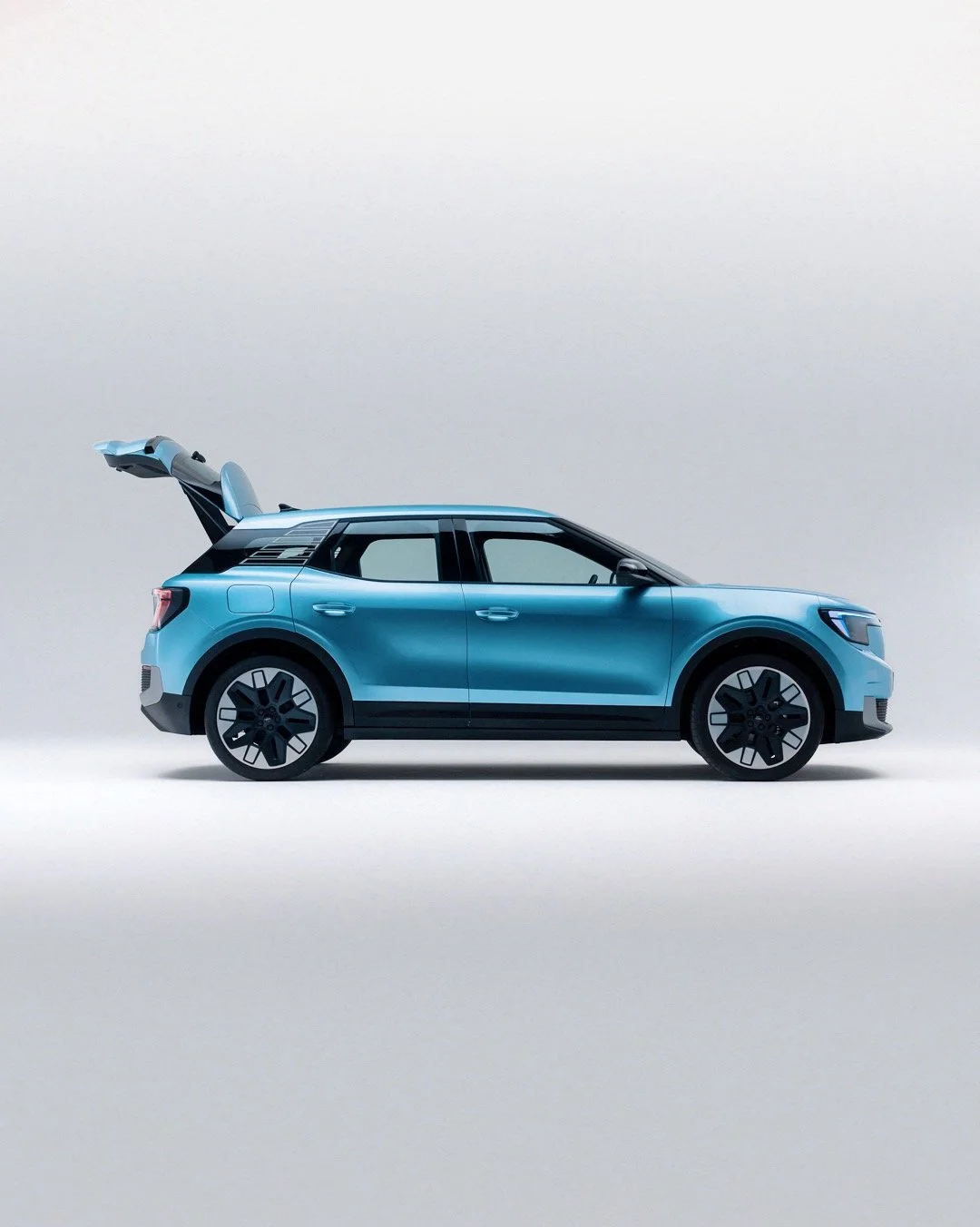 Side view of a blue compact SUV with rear hatch open on a plain white background.