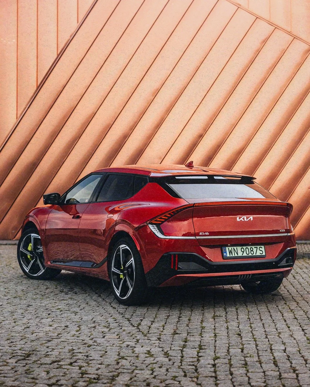 Red Kia EV6 electric car parked on cobblestone street in front of a modern metallic building