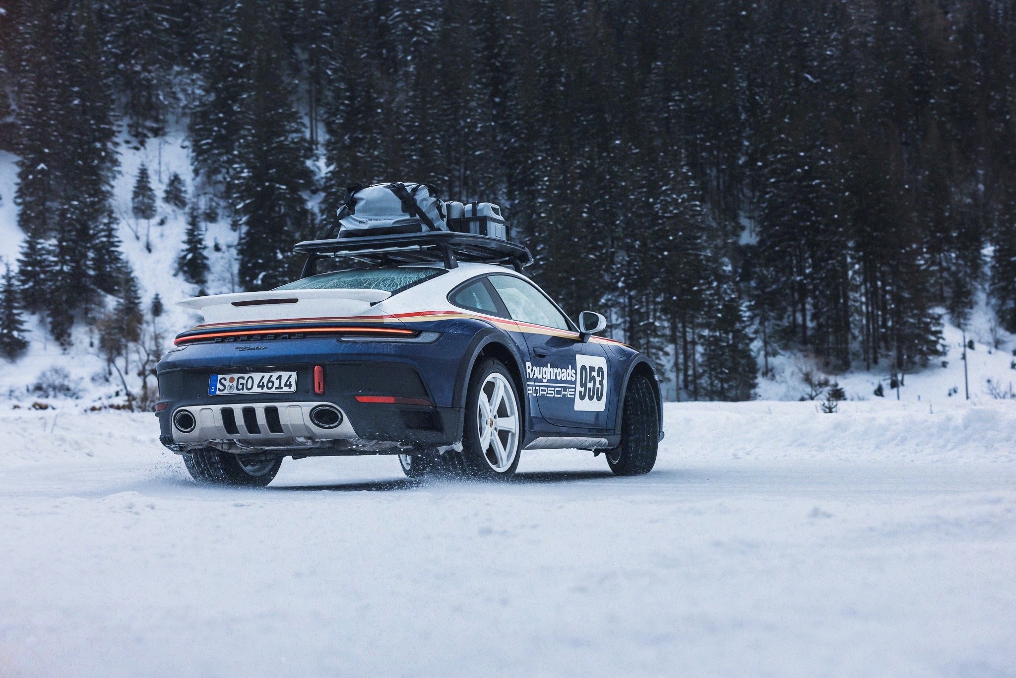A sports car driving on a snowy road with snow-covered trees in the background.