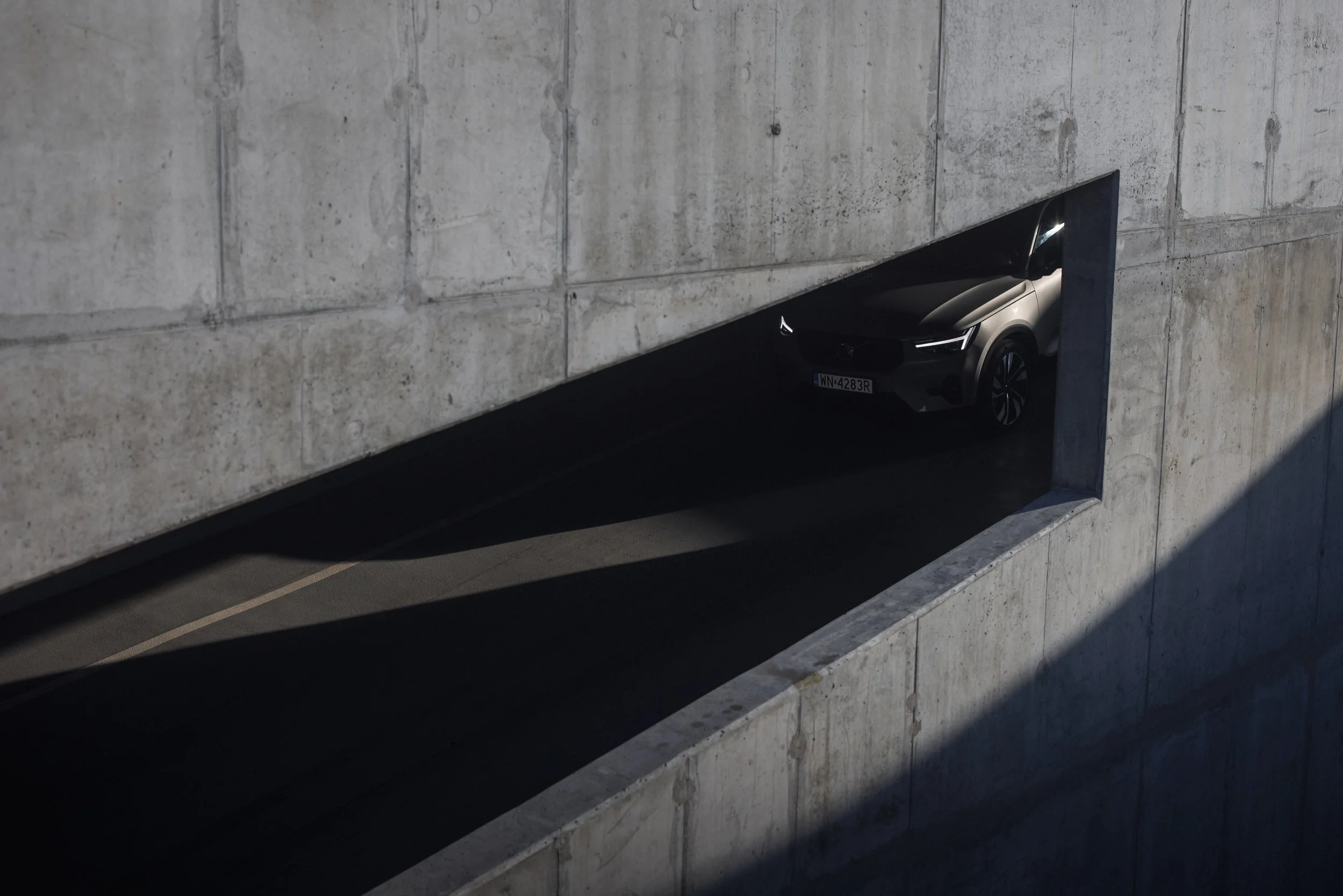 A car parked in an underground concrete parking garage, seen through a rectangular opening in the wall.