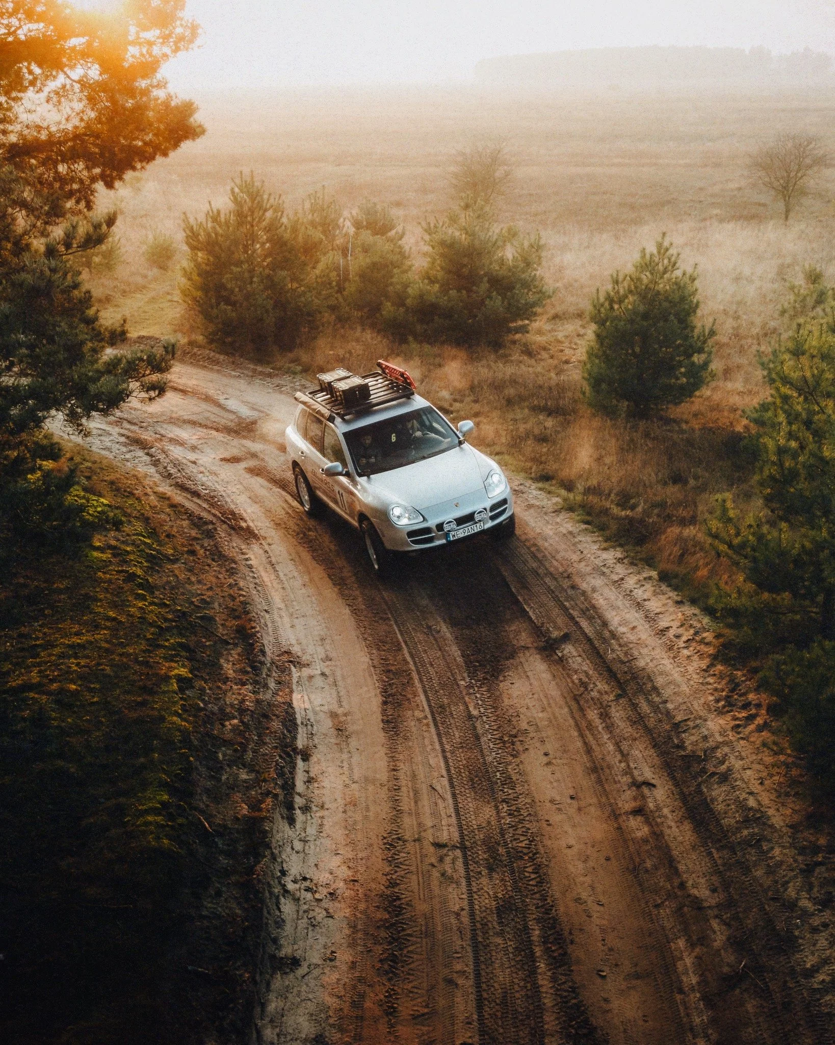 A silver SUV driving on a dirt road through a rural landscape with trees and fog in the background.