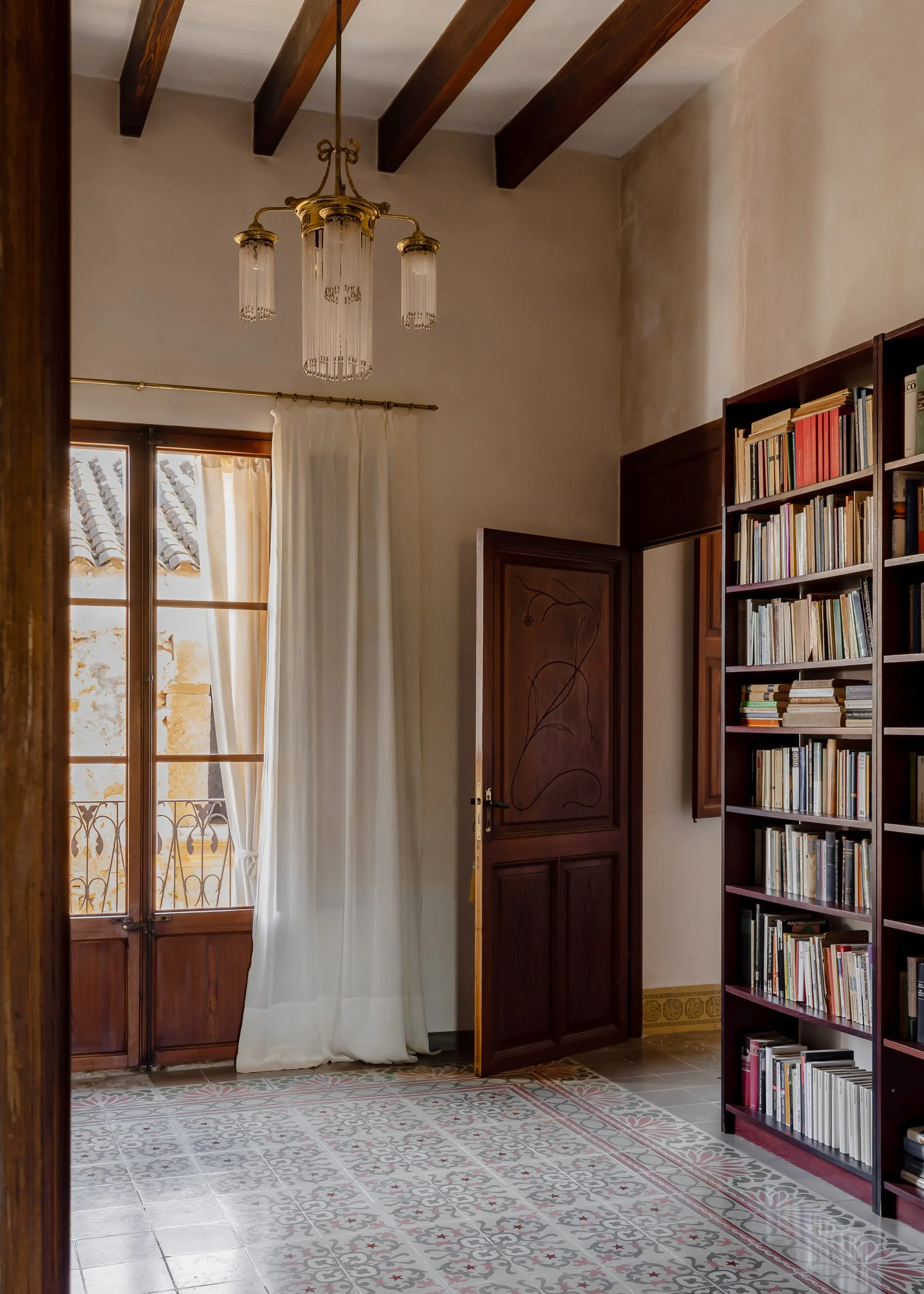 Interior hallway with patterned tiles, bookshelves, and natural light