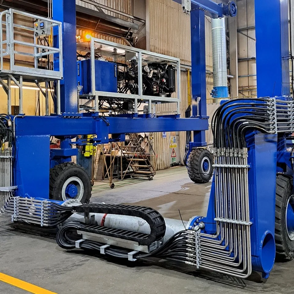 Large industrial blue machine with hydraulic hoses and metal framework in a factory setting.