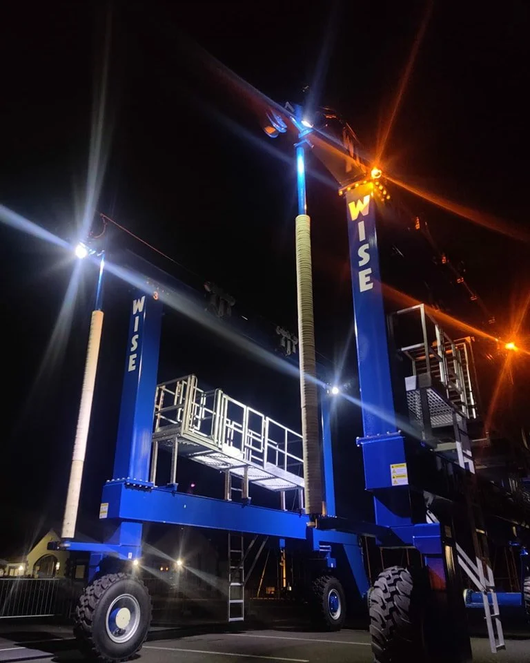 A large blue WISE Slipway Hoist at night with the hoists onboard lights illuminating the machine.