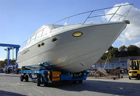Large white yacht on a WISE Boat Transporter at a boatyard with machinery around.
