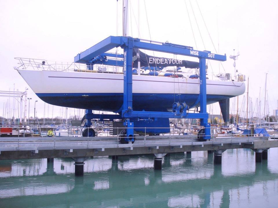 A sailboat named Endeavor is lifted out of the water by a large blue boat hoist at a marina.