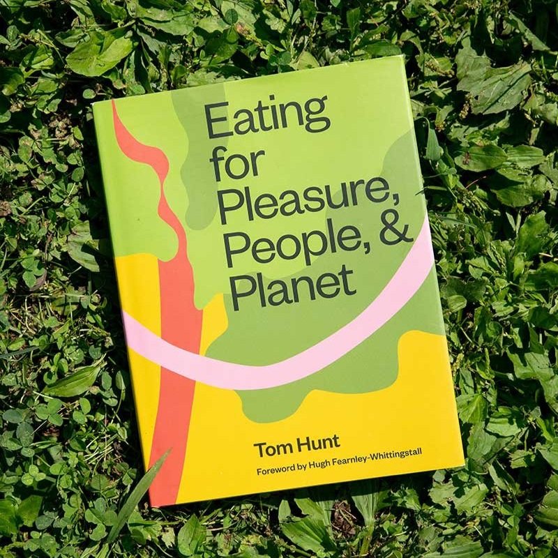 The cover of the book Eating for Pleasure, People & Planet lies in the brightly lit grass.