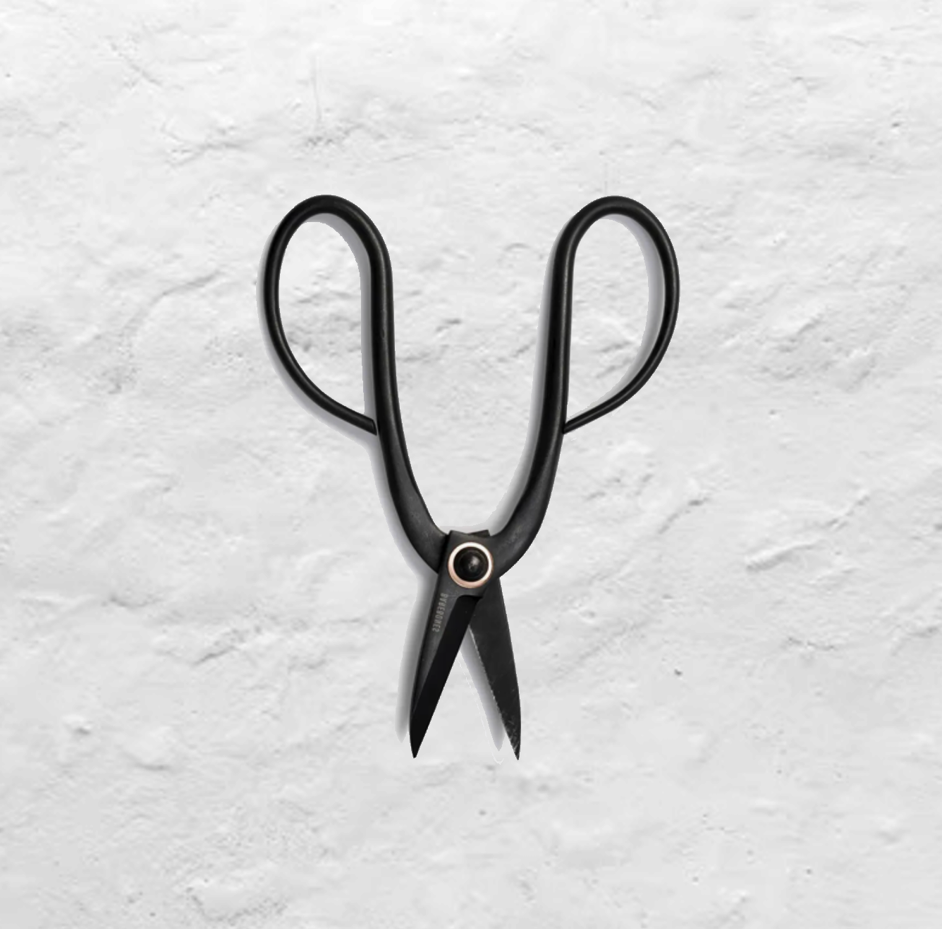 A black pair of pruning shears lie open on a white plaster background.