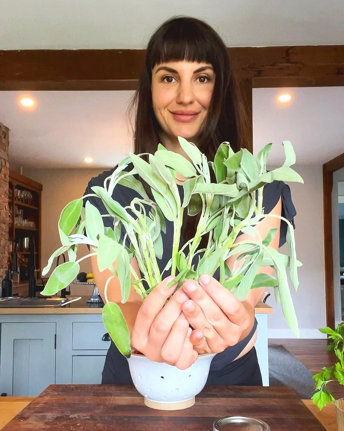 Kristen stands in her kitchen holding a bunch of just-picked sages leaves in her hands.