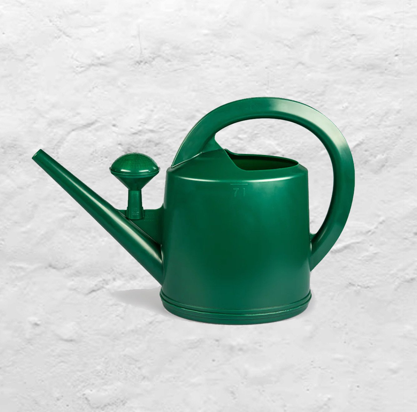 A dark green Dramm watering can with the water nozzle sitting on the body of the can sits on a white plaster background.
