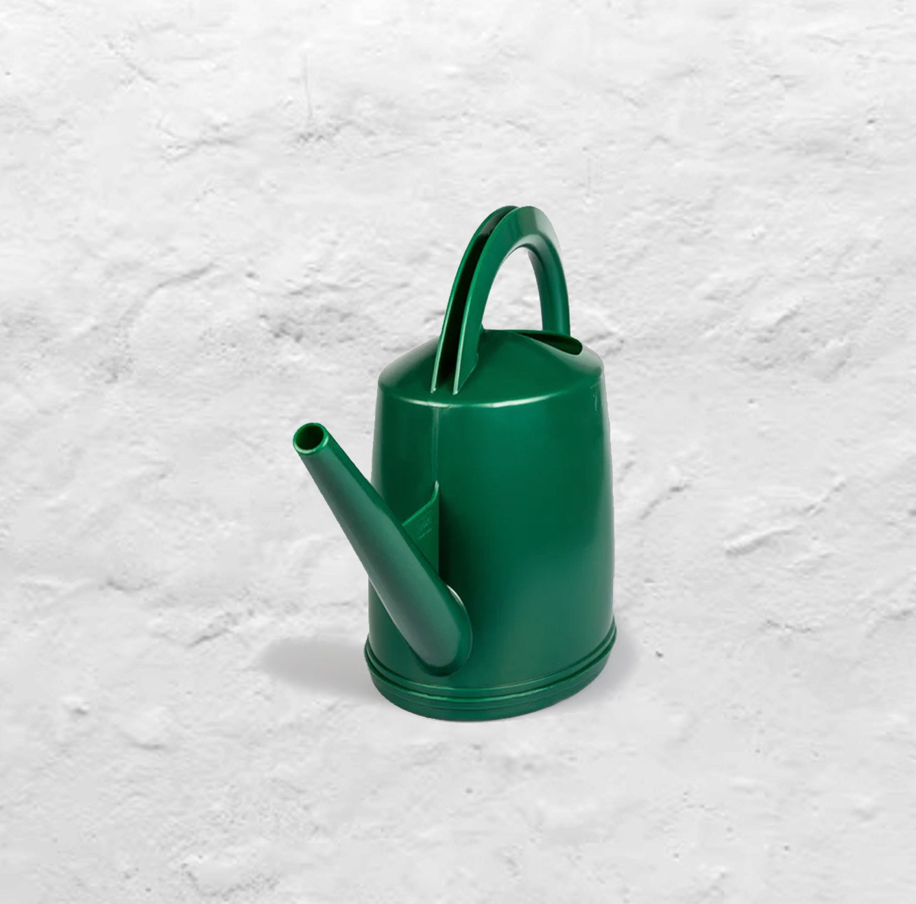 A dark green Dramm watering can with the water nozzle detached sits on a white plaster background.