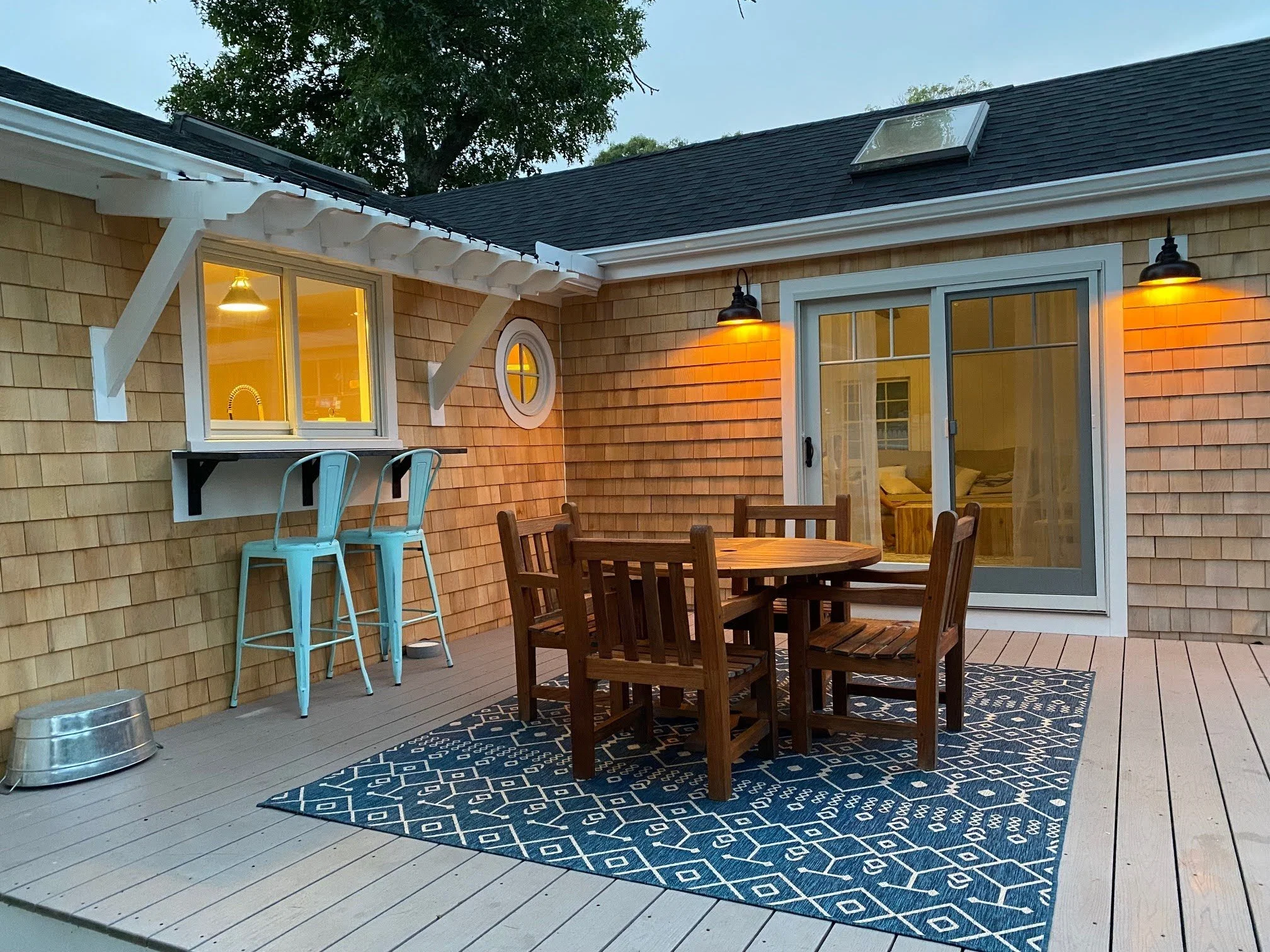 Shingle-style Cape Cod home with an outdoor dining deck, sliding glass doors, black sconces, and turquoise bar stools.