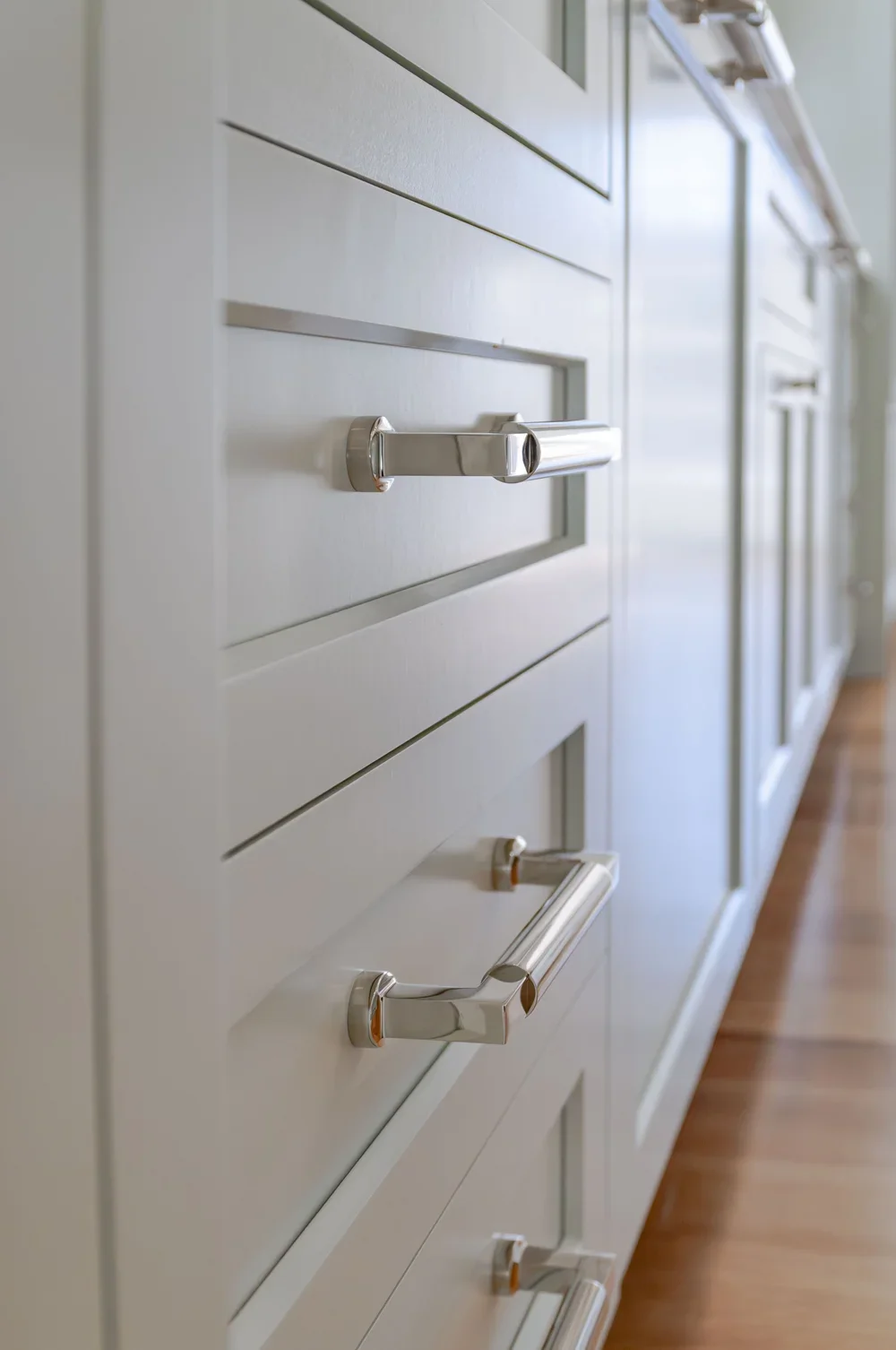 Polished cabinet hardware and pale millwork bring refined detail to this high-end Cape Cod renovation kitchen.