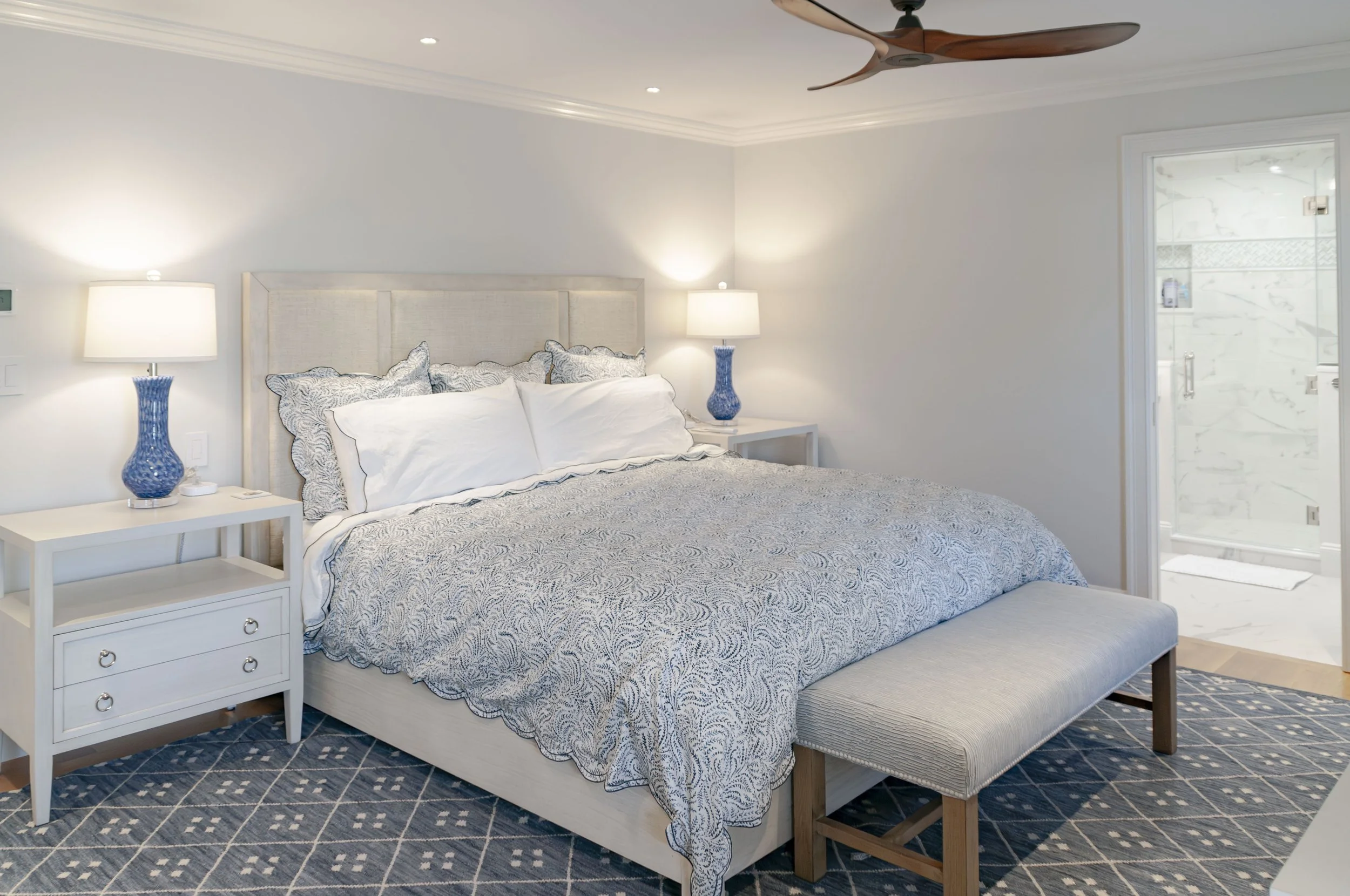 Luxury Cape Cod bedroom with blue coastal bedding, custom home finishes, and adjoining marble-look bathroom.