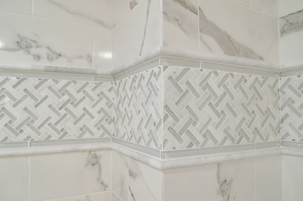 Woven accent tile and marble-look surround bring high-end Cape Cod renovation detail to this shower wall.