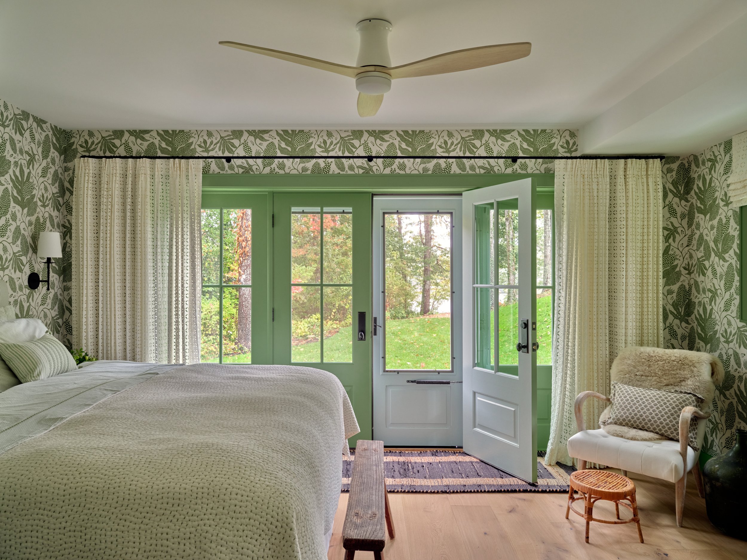 French doors and botanical wallpaper bring natural light into this Cape Cod bedroom with hardwood floors and custom coastal finishes.