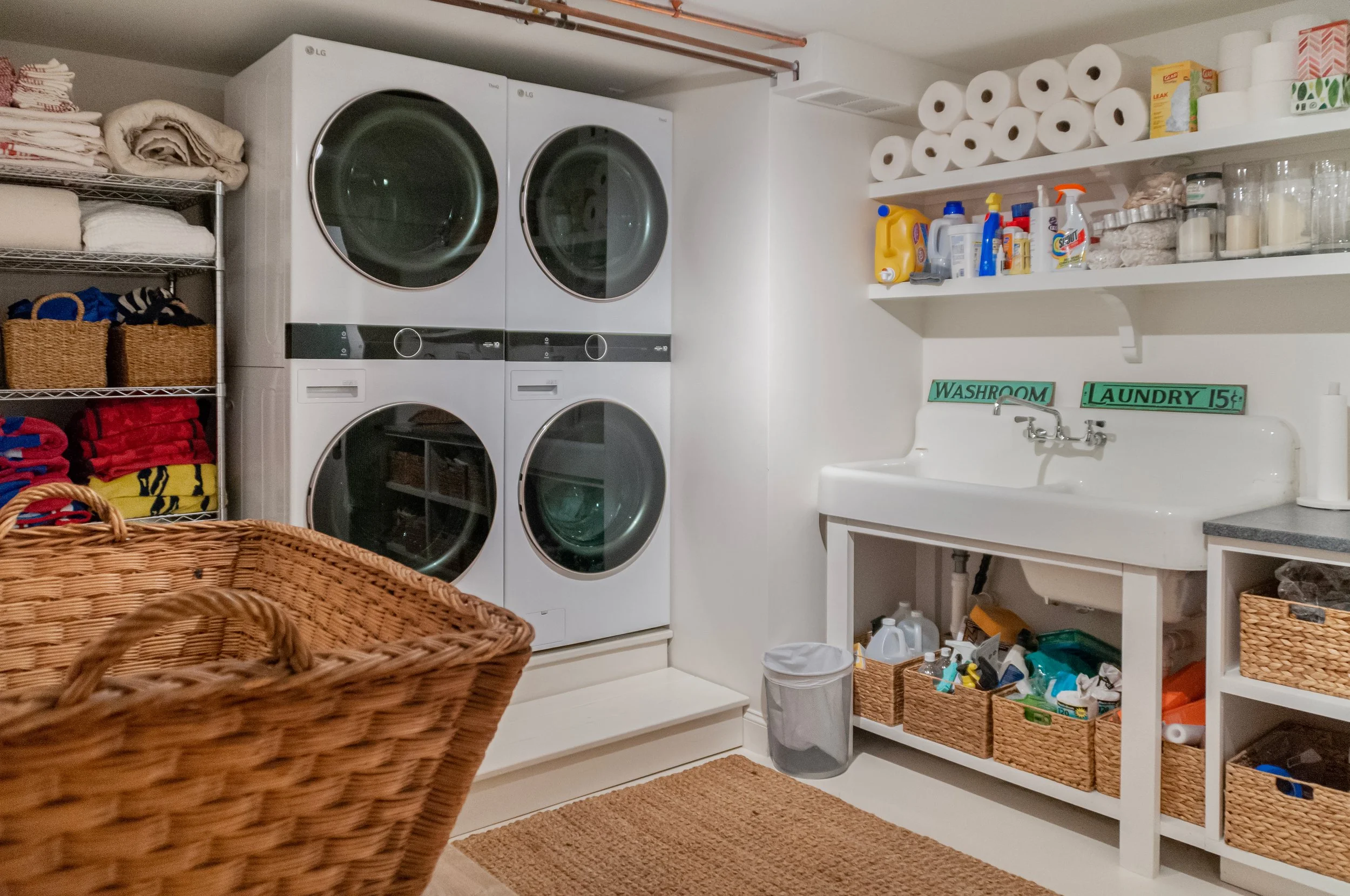 Laundry room with stacked washers, utility sink, open shelving, and Cape Cod home renovation storage.