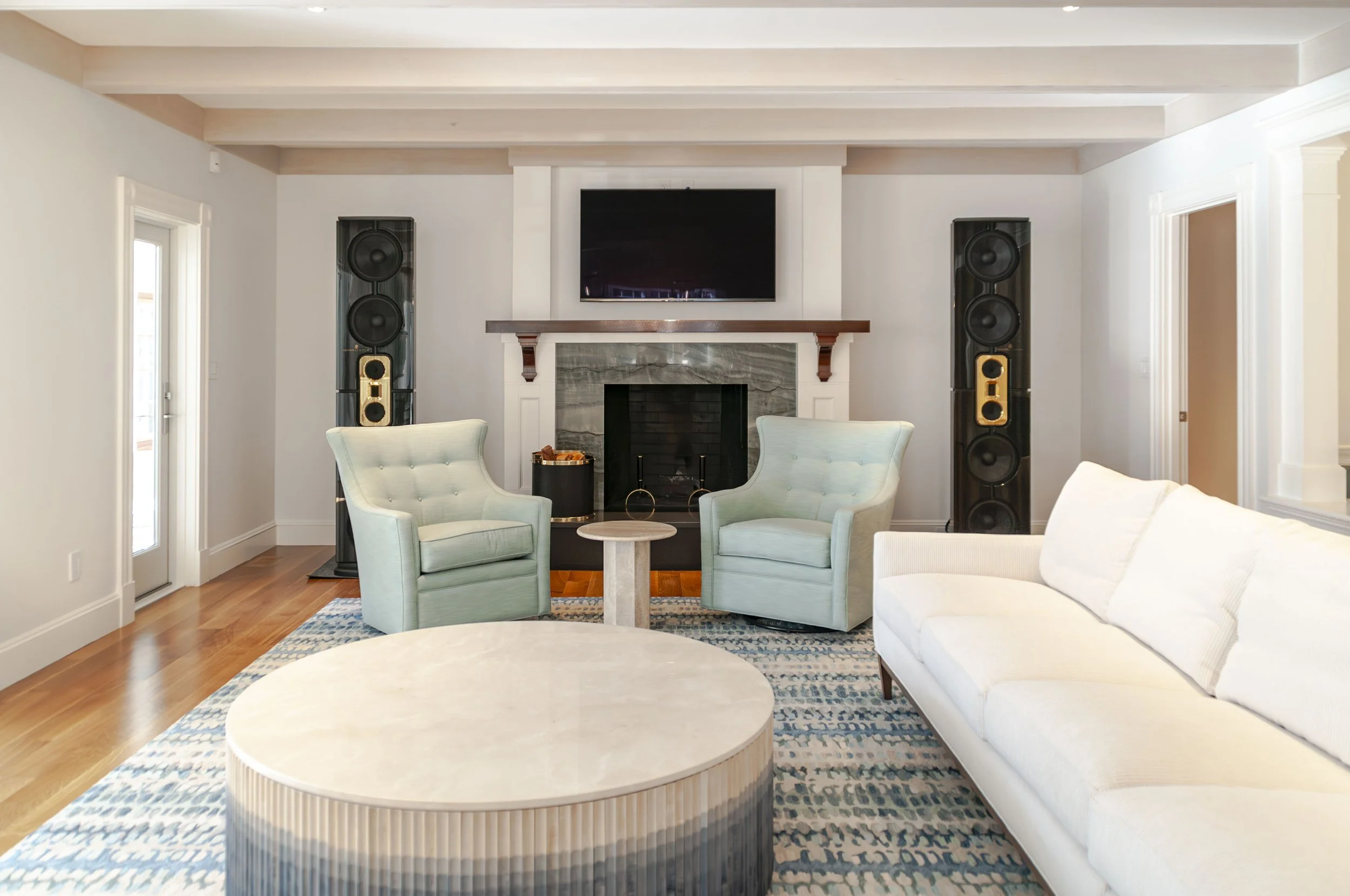 Open Cape Cod living area with white sectional, beamed ceiling, and kitchen with soft green cabinetry beyond.