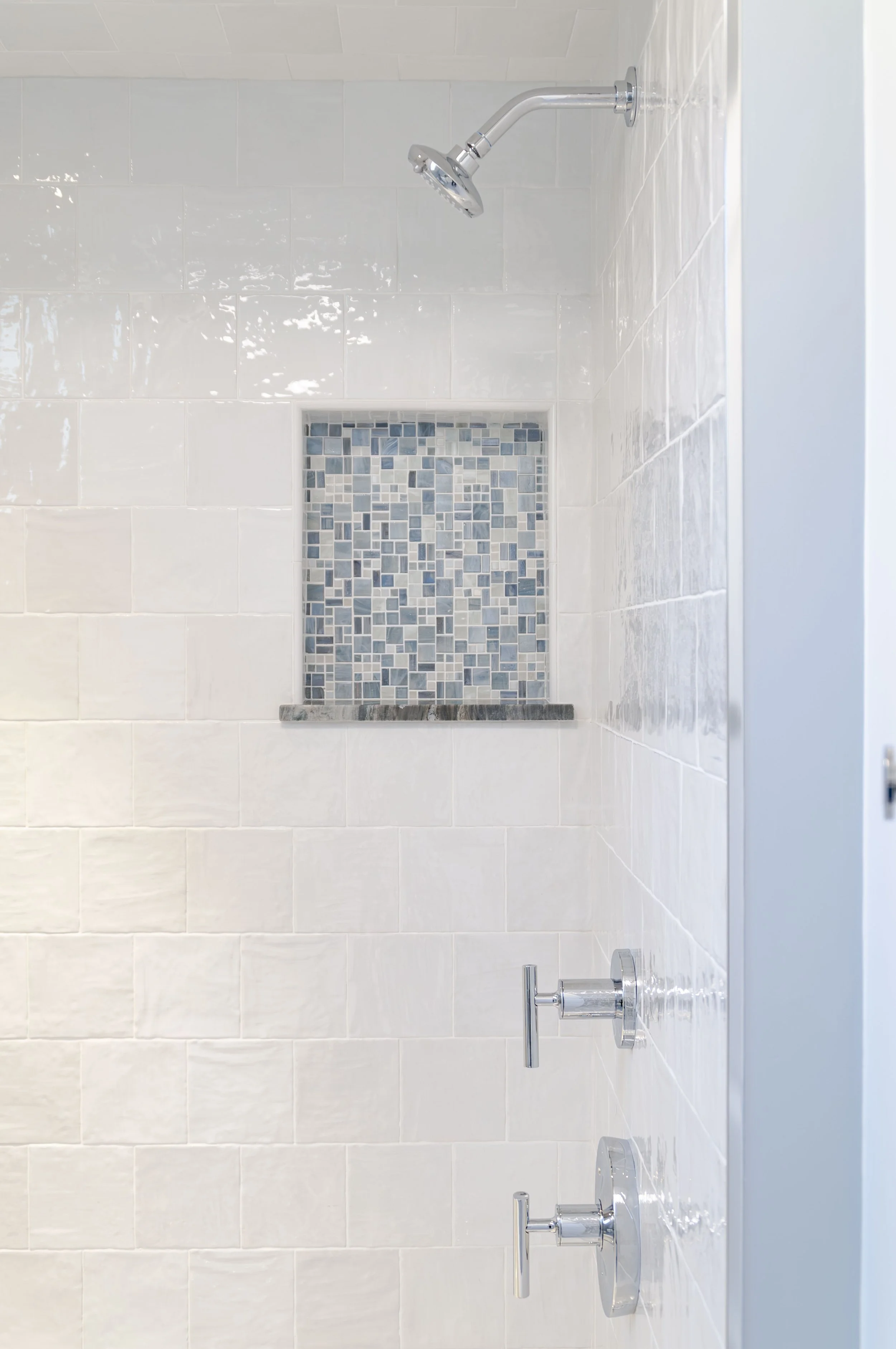 Cape Cod shower with glossy white tile, blue mosaic niche, polished fixtures, and clean coastal detailing.