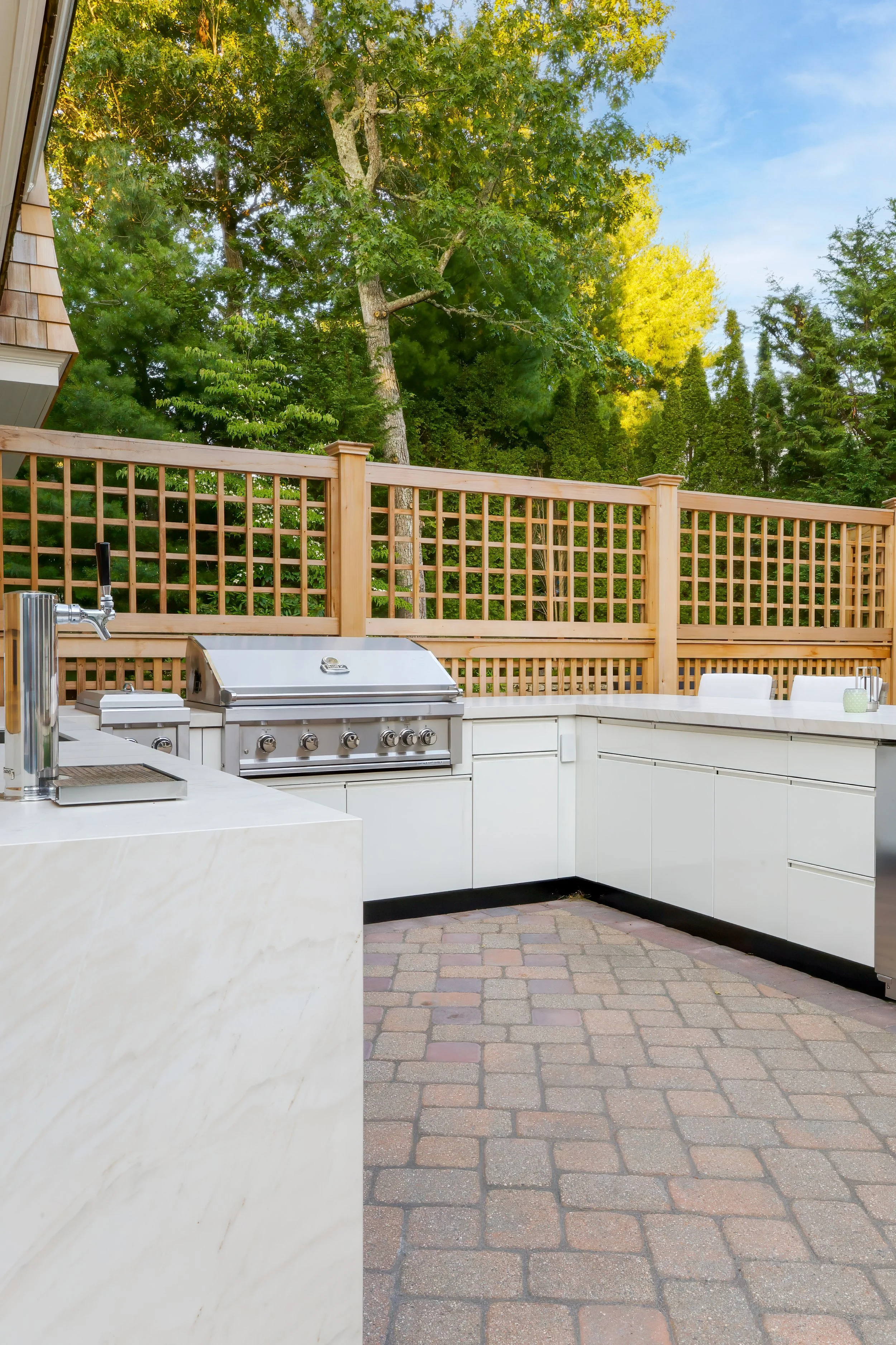 Marble-look counters, white storage, and a built-in grill shape this Cape Cod patio kitchen.