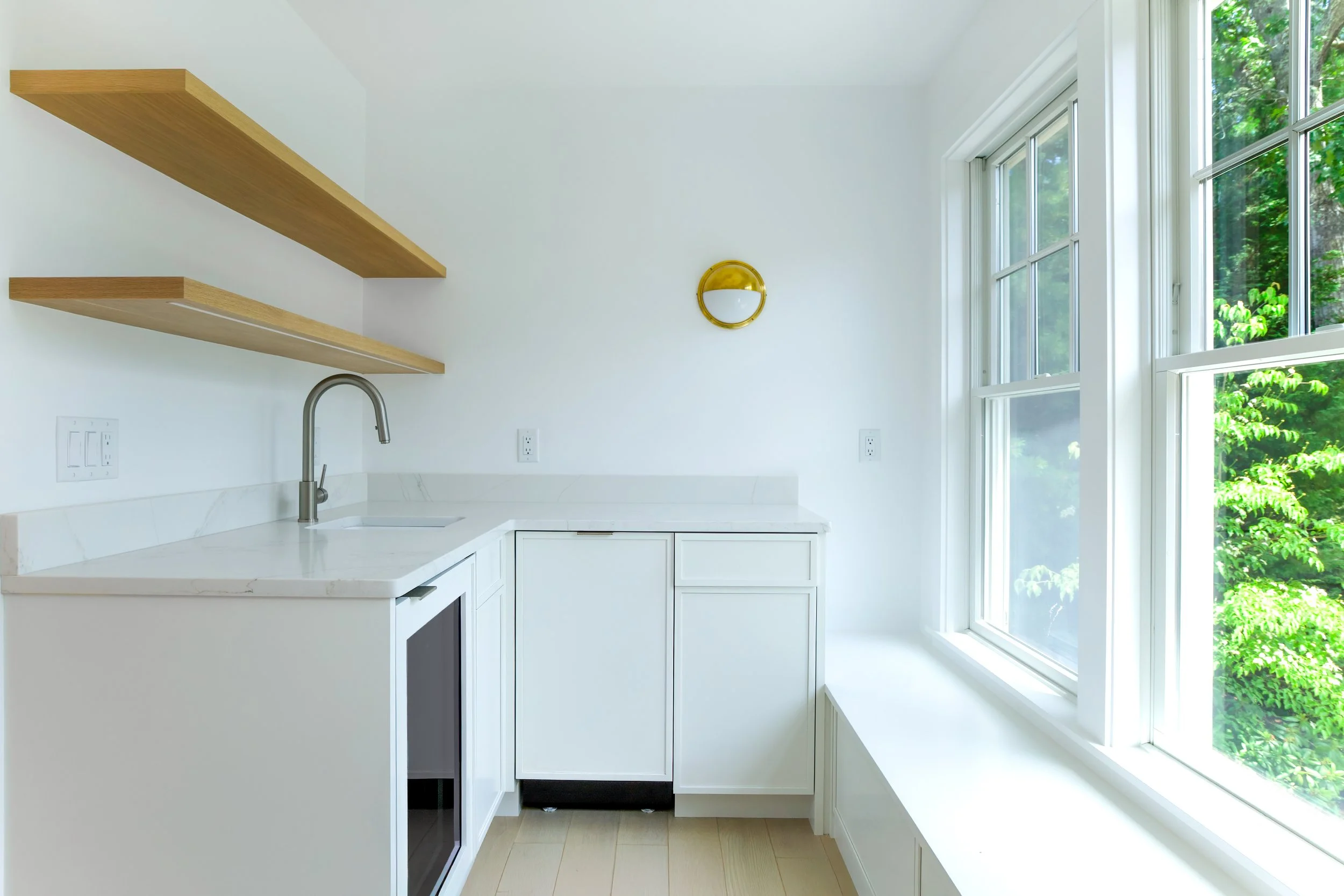 Windowed kitchenette with floating wood shelves, white cabinetry, and coastal guest suite design details.