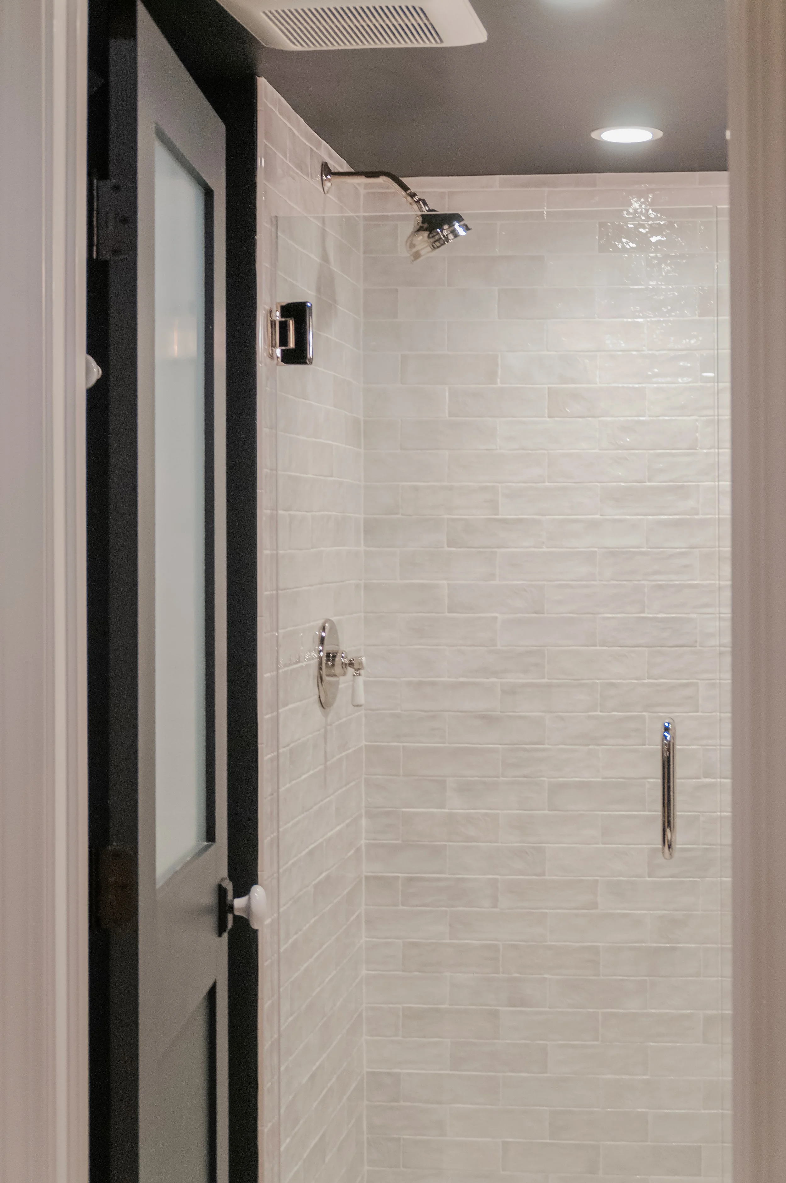 Glossy white tile shower with black trim, polished fixtures, and coastal bathroom renovation details.