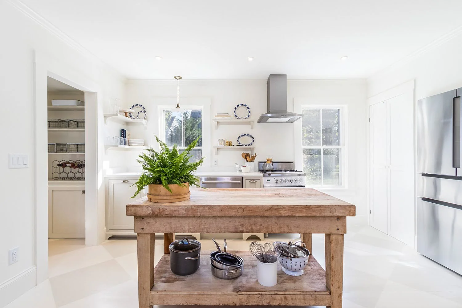 Bright custom coastal home kitchen with a rustic wood island, stainless appliances, white cabinetry, and Cape Cod style.