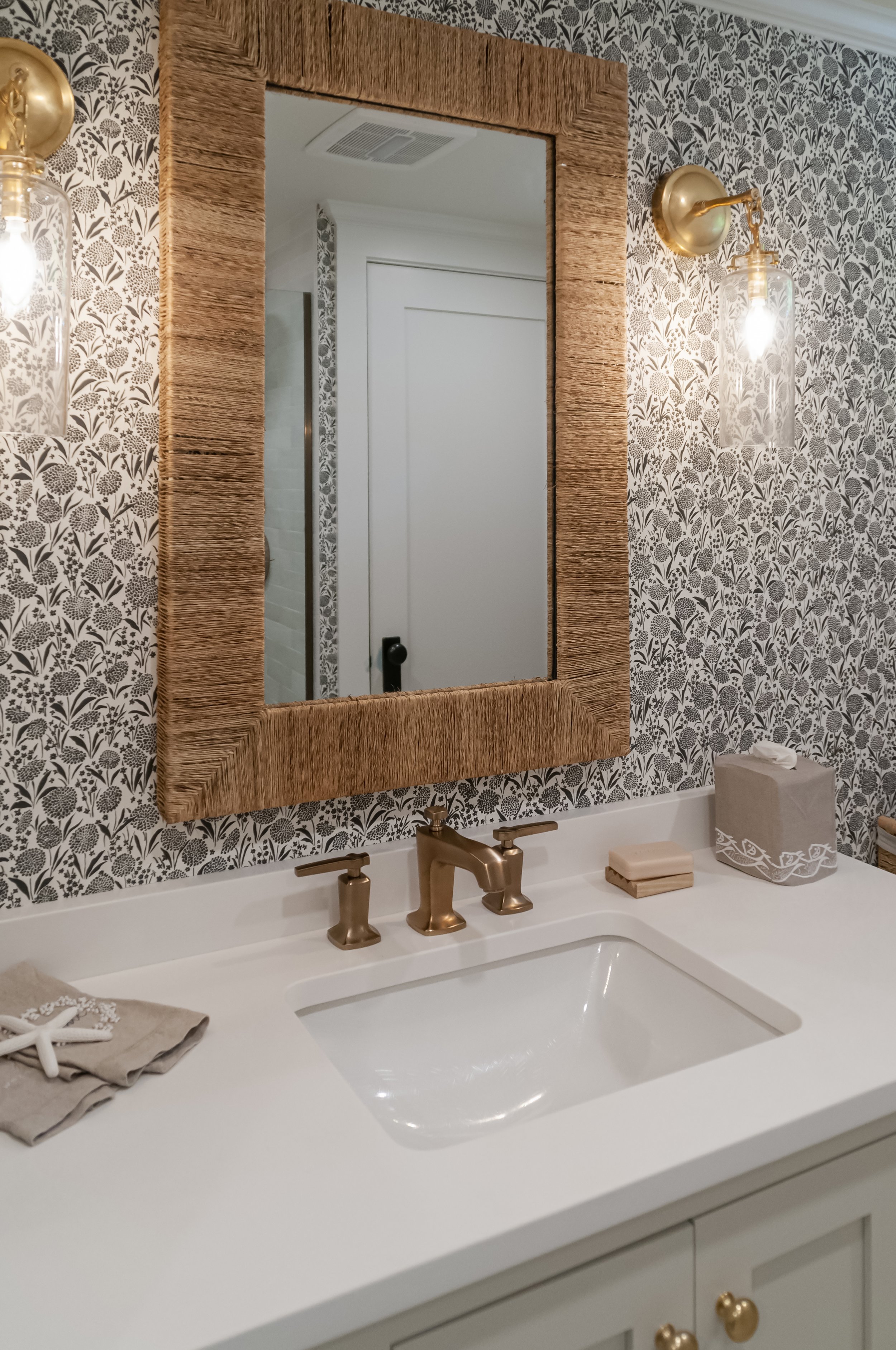 Patterned wallpaper and brass fixtures add custom coastal home character to this polished powder bath.