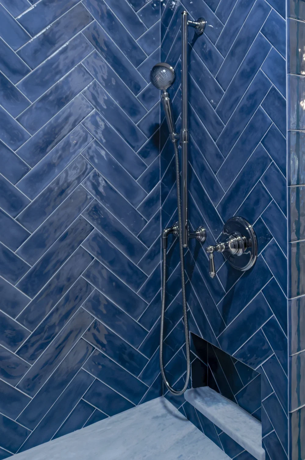 Blue herringbone tile and chrome fixtures showcase high-end Cape Cod renovation detail in this glass shower.