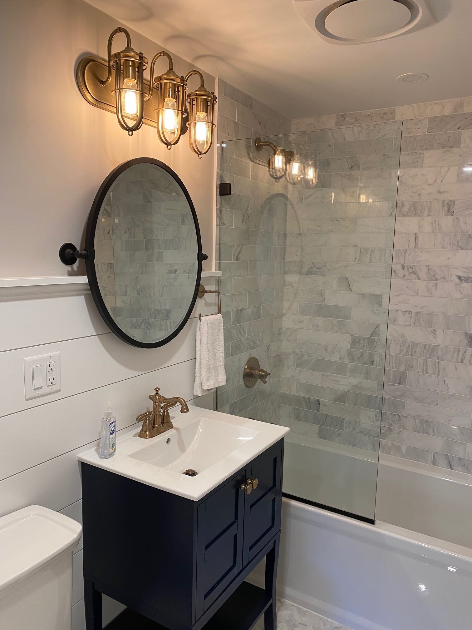 Nautical sconces and marble tile bring custom coastal home character to this navy vanity bath.