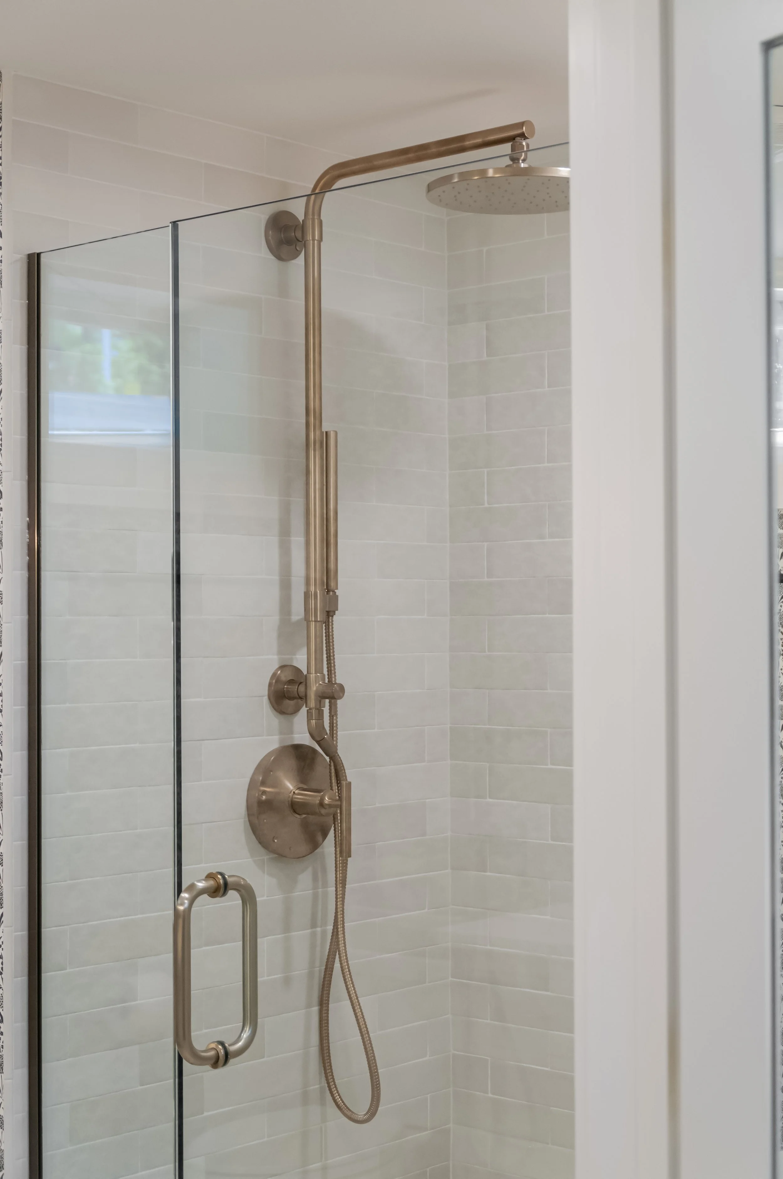 Brushed bronze fixtures and pale tile bring luxury home builder in Osterville detail to this glass shower.