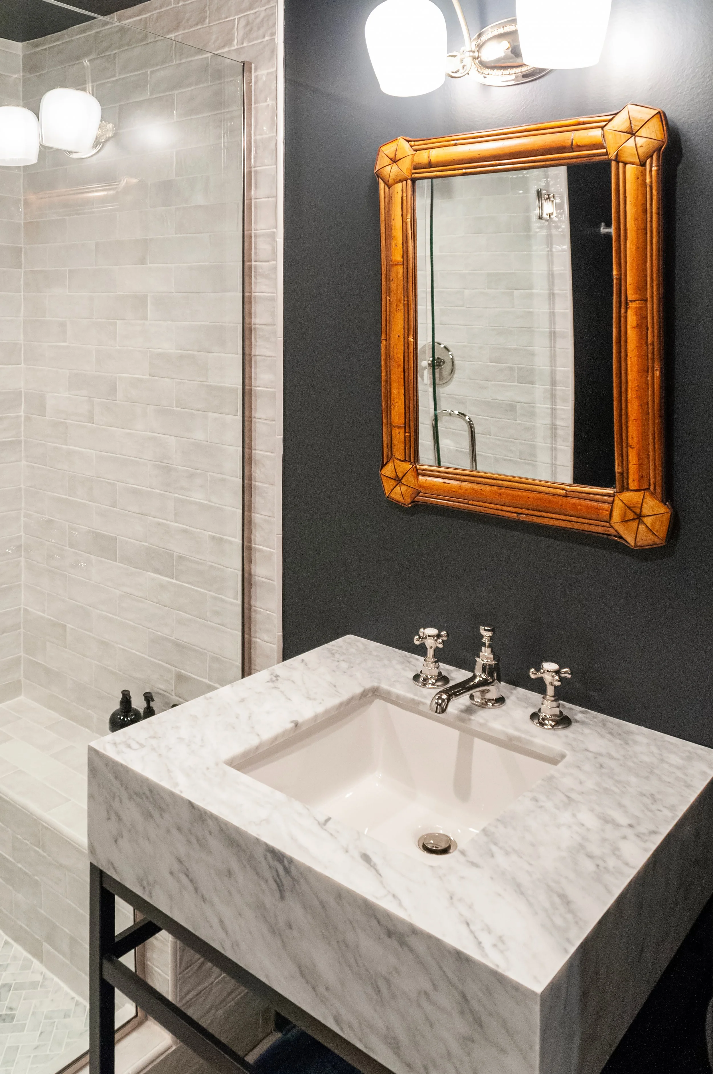 Marble sink, bamboo mirror, and glass shower bring polished Cape Cod bathroom design to this space.