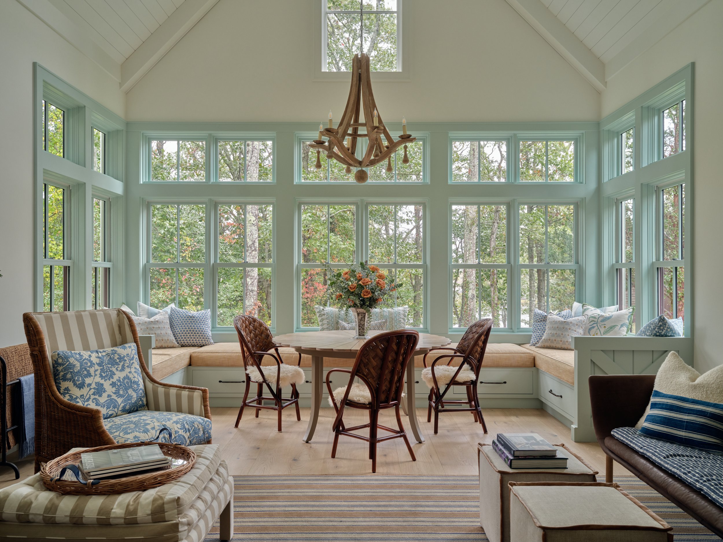 Framed by floor-to-ceiling windows, this Sea View Builders sunroom features custom window benches, vaulted ceilings, and panoramic Cape Cod woodland views.
