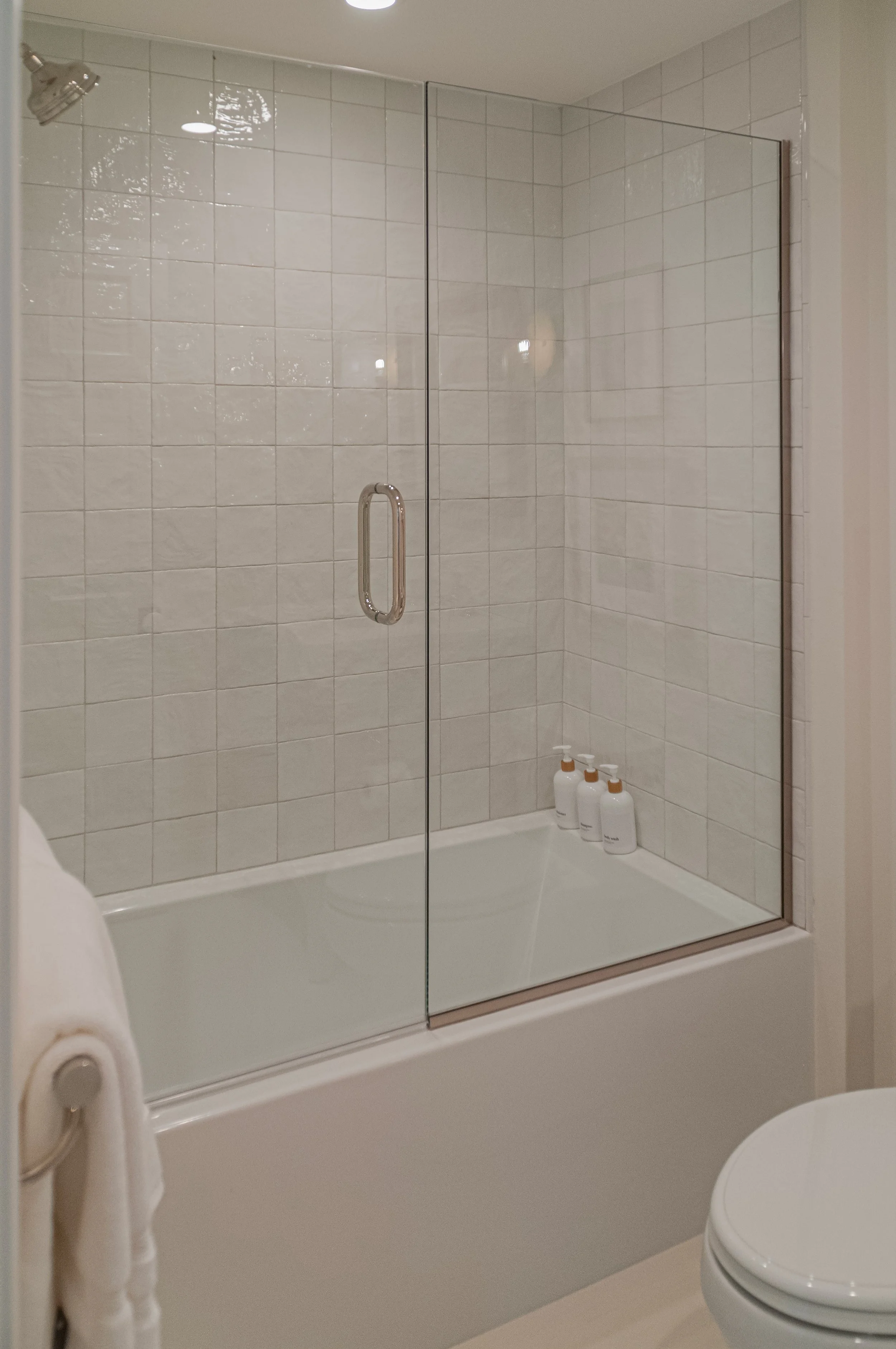 Glass shower bathroom renovation with glossy white tile, polished hardware, and clean coastal styling.