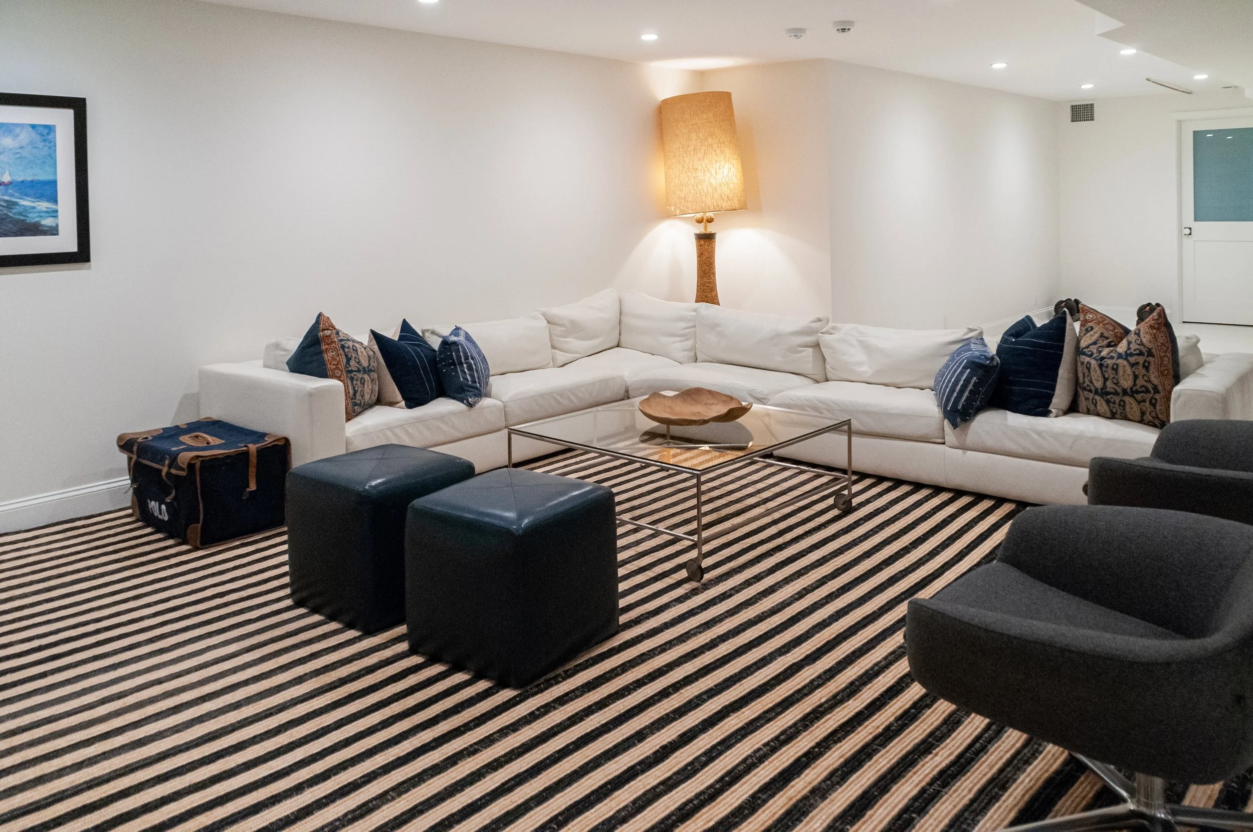 Lower-level lounge with white sectional, striped rug, navy pillows, and entertaining space.