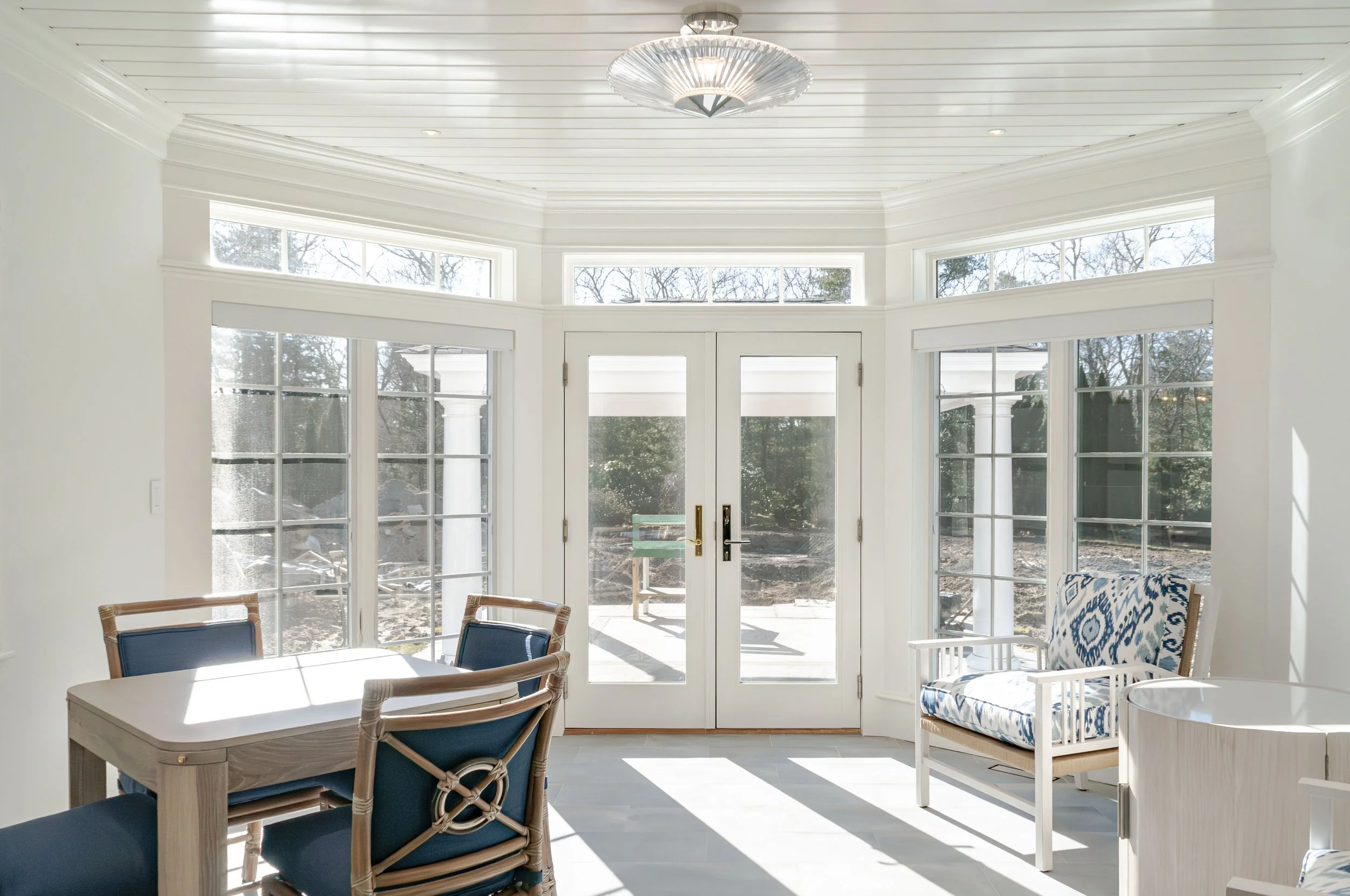 Cape Cod kitchen with marble island, soft green cabinetry, bright window views, and polished pendant lighting.