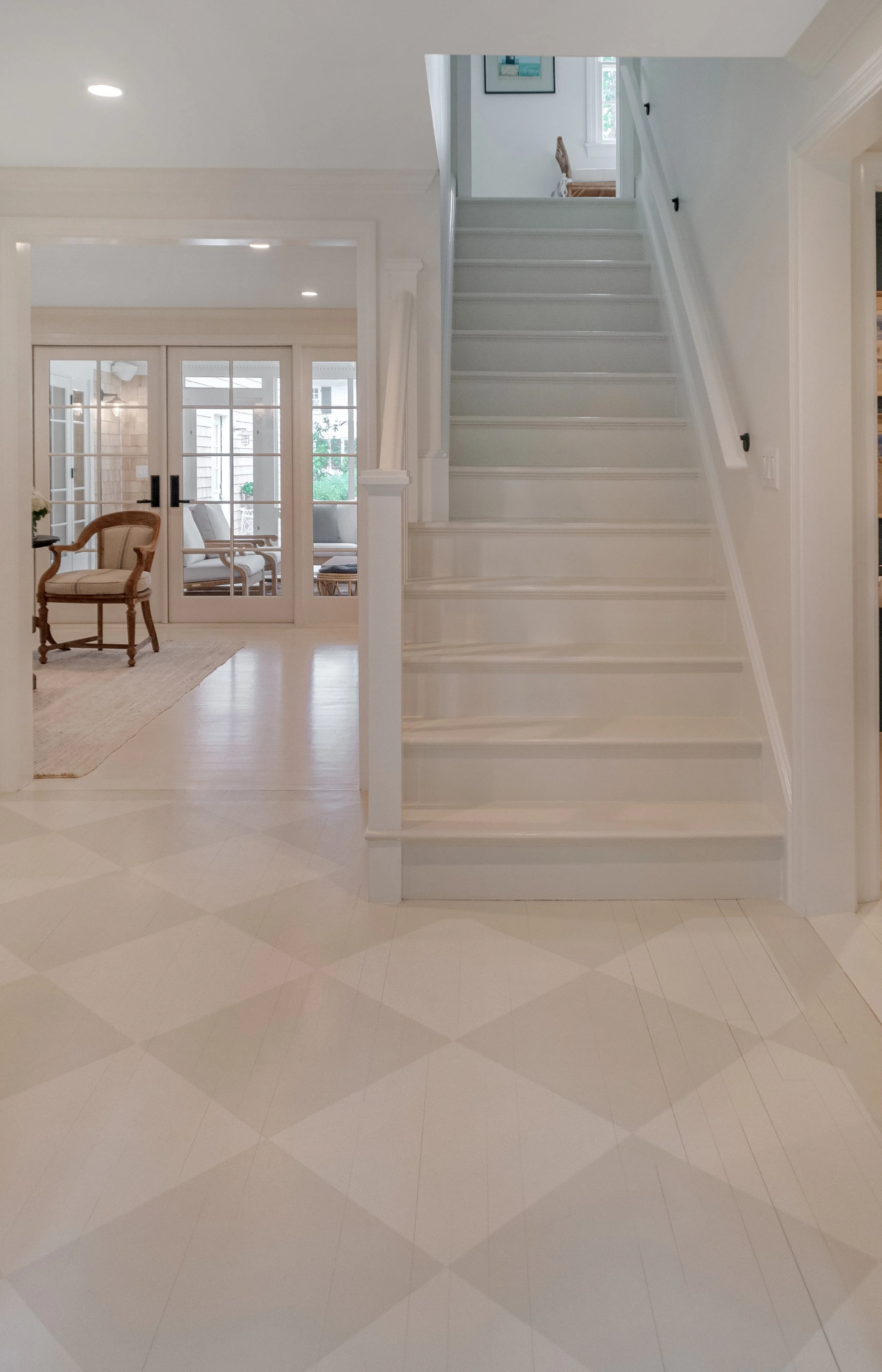 Painted staircase and checkered floor add classic detail to this Cape Cod home renovation entryway.