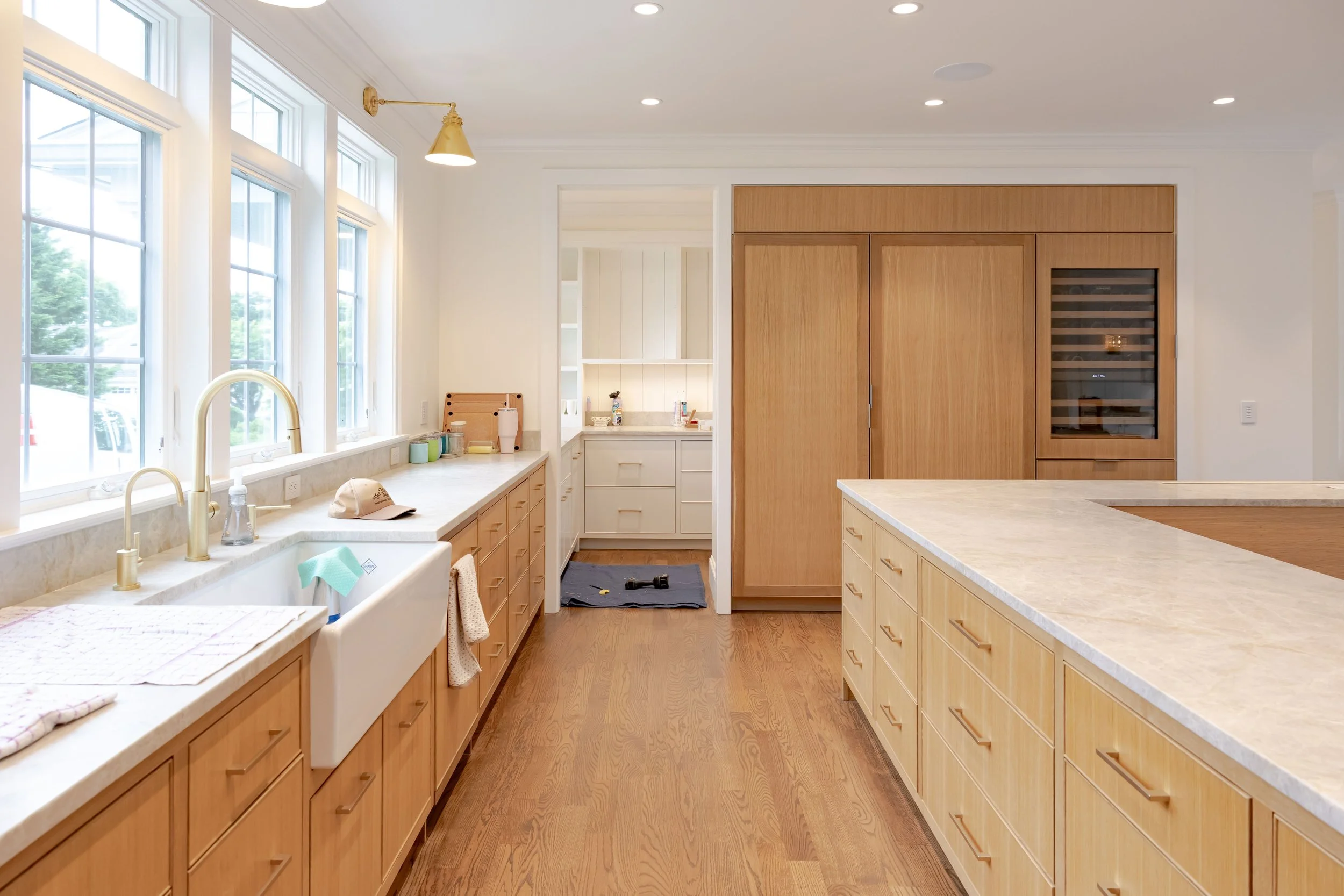 Natural white oak cabinetry, oversized kitchen island, integrated wine storage, farmhouse sink, and quartz countertops create a bright, functional Cape Cod kitchen.