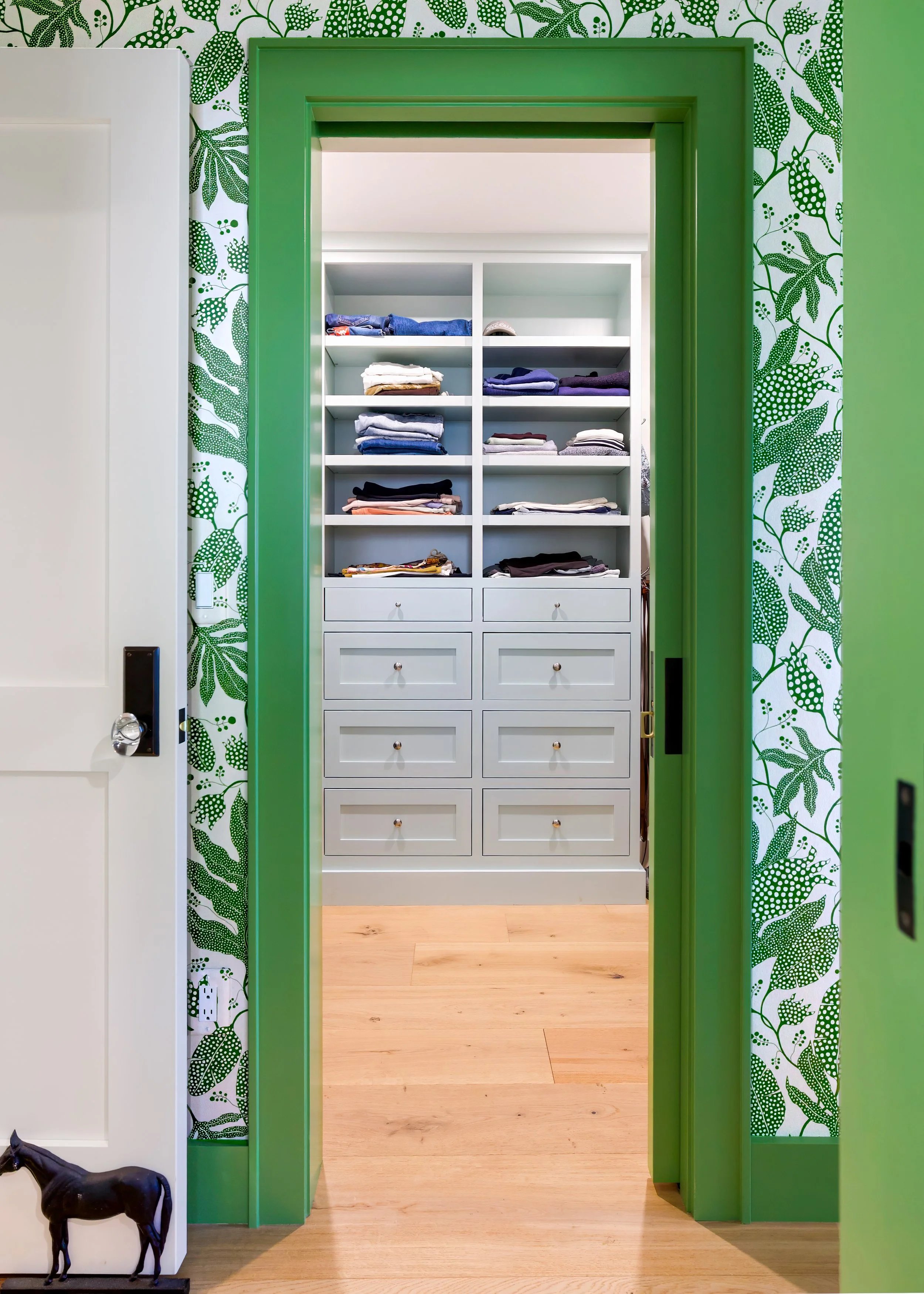 Green-trimmed doorway with botanical wallpaper opens to a built-in closet in a Cape Cod interior.