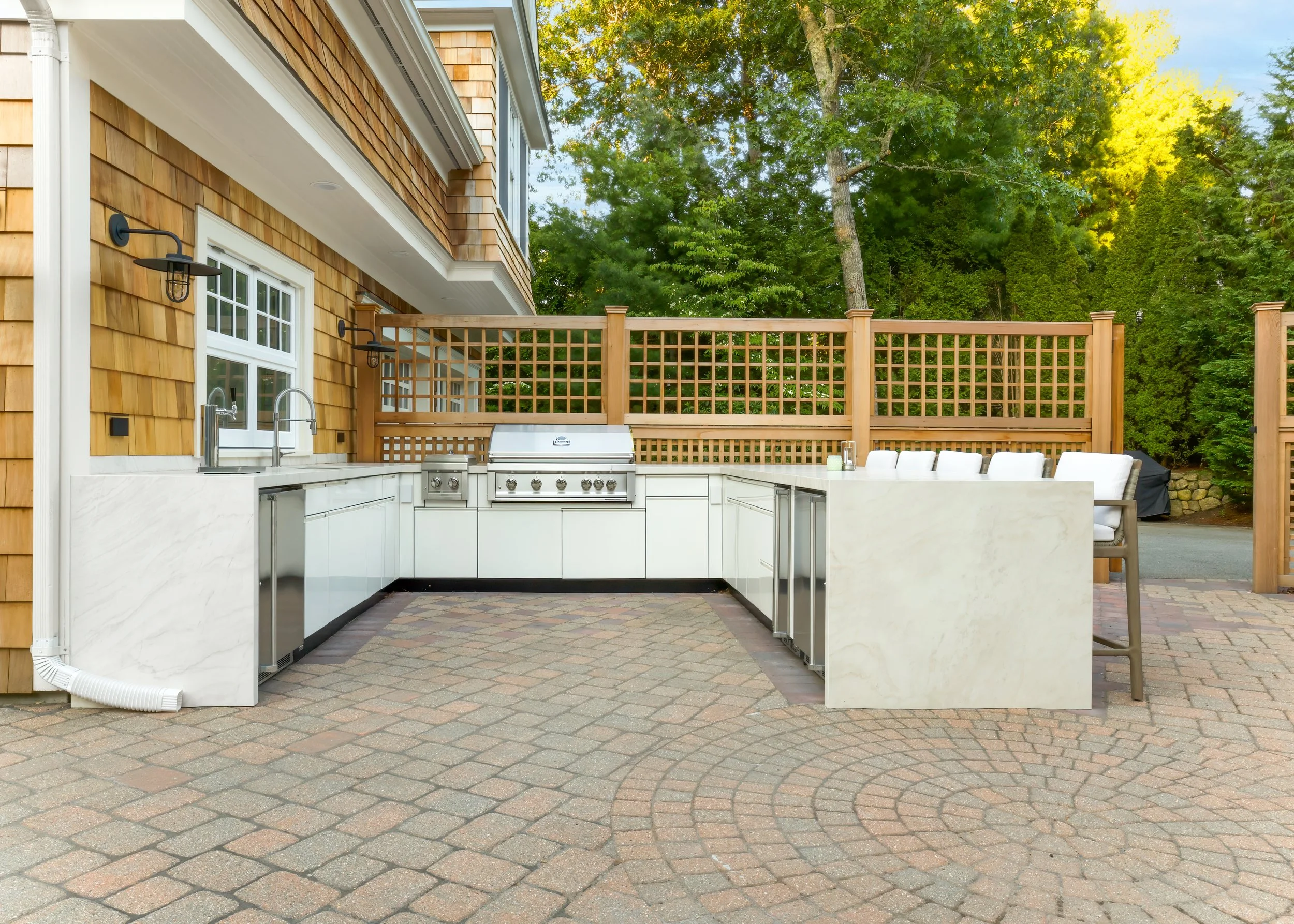 Outdoor kitchen with grill, bar seating, cedar lattice, and stone patio for Cape Cod backyard entertaining.
