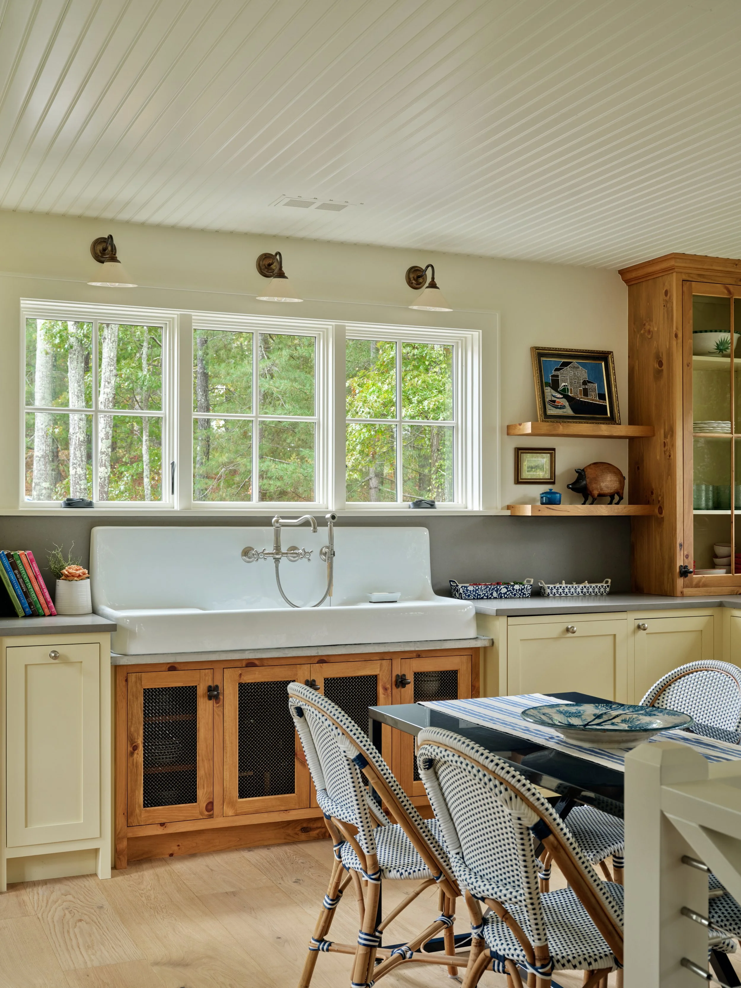 Bathed in natural light, this Sea View Builders kitchen features a farmhouse sink, custom cabinetry, wood shelving, and classic Cape Cod craftsmanship.