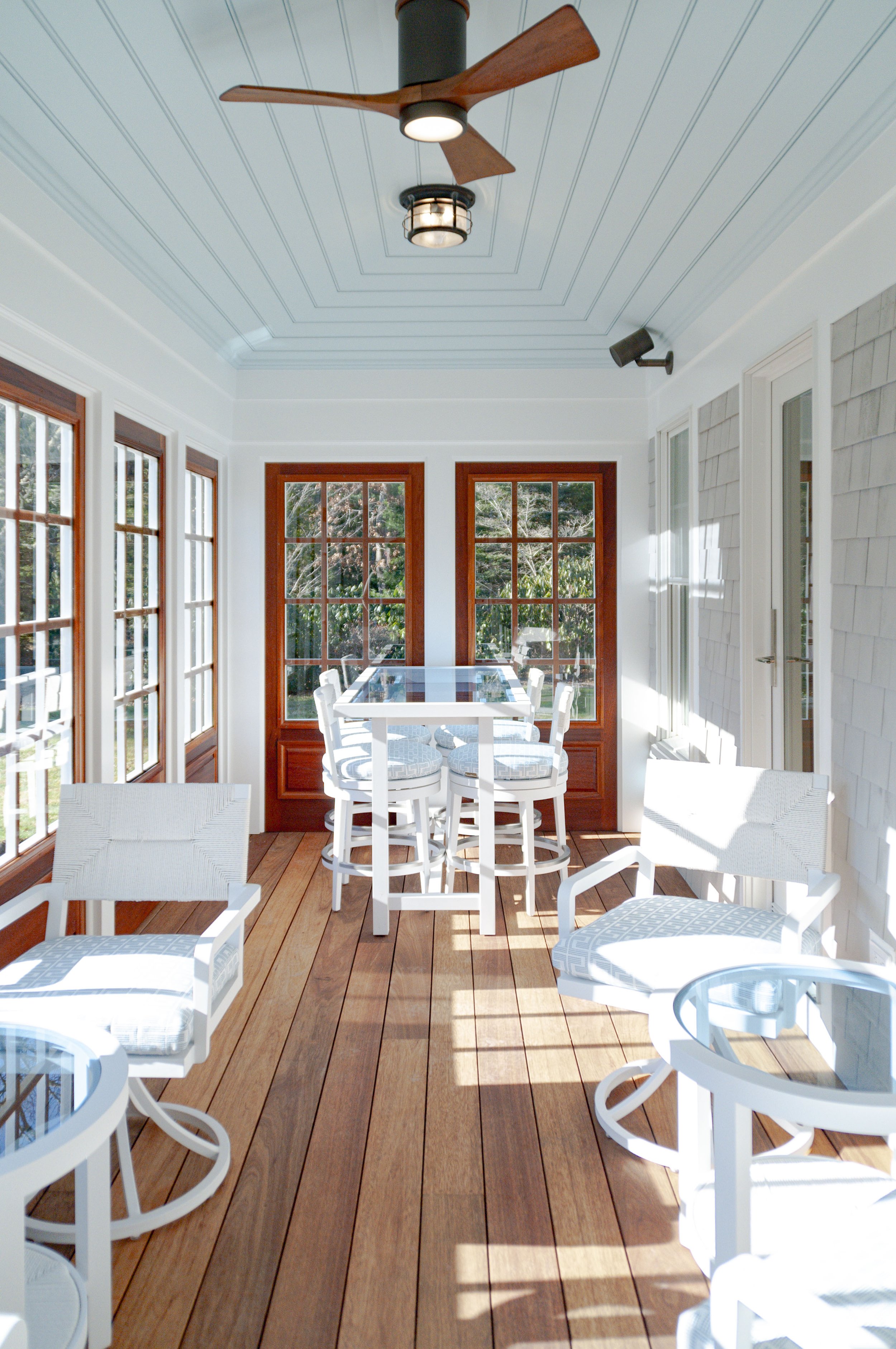 Cape Cod screened porch with wood decking, blue beadboard ceiling, white seating, and custom coastal home details.