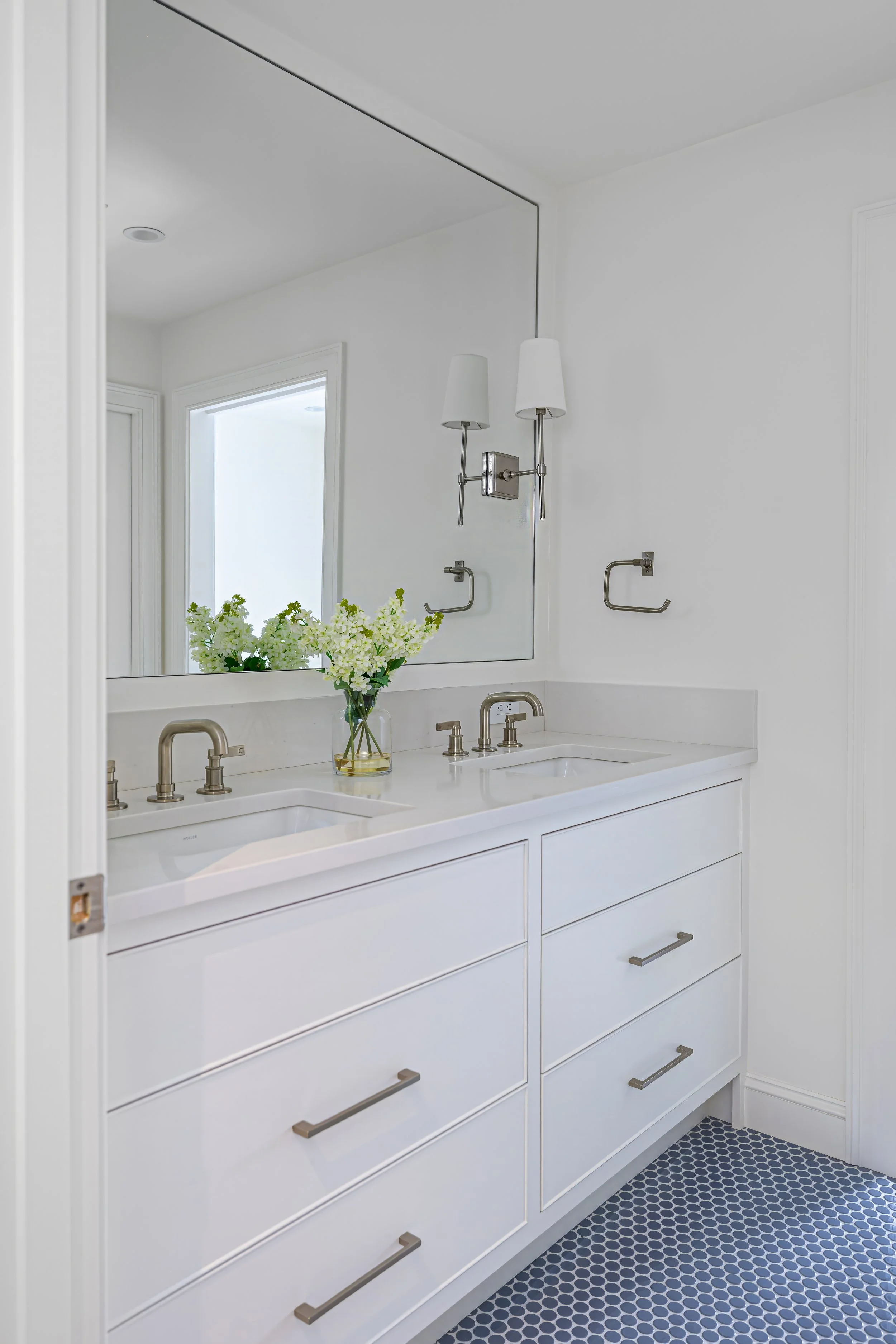 Custom Cape Cod bathroom featuring a double vanity, quartz countertops, oversized mirror, polished nickel fixtures, and timeless white cabinetry.
