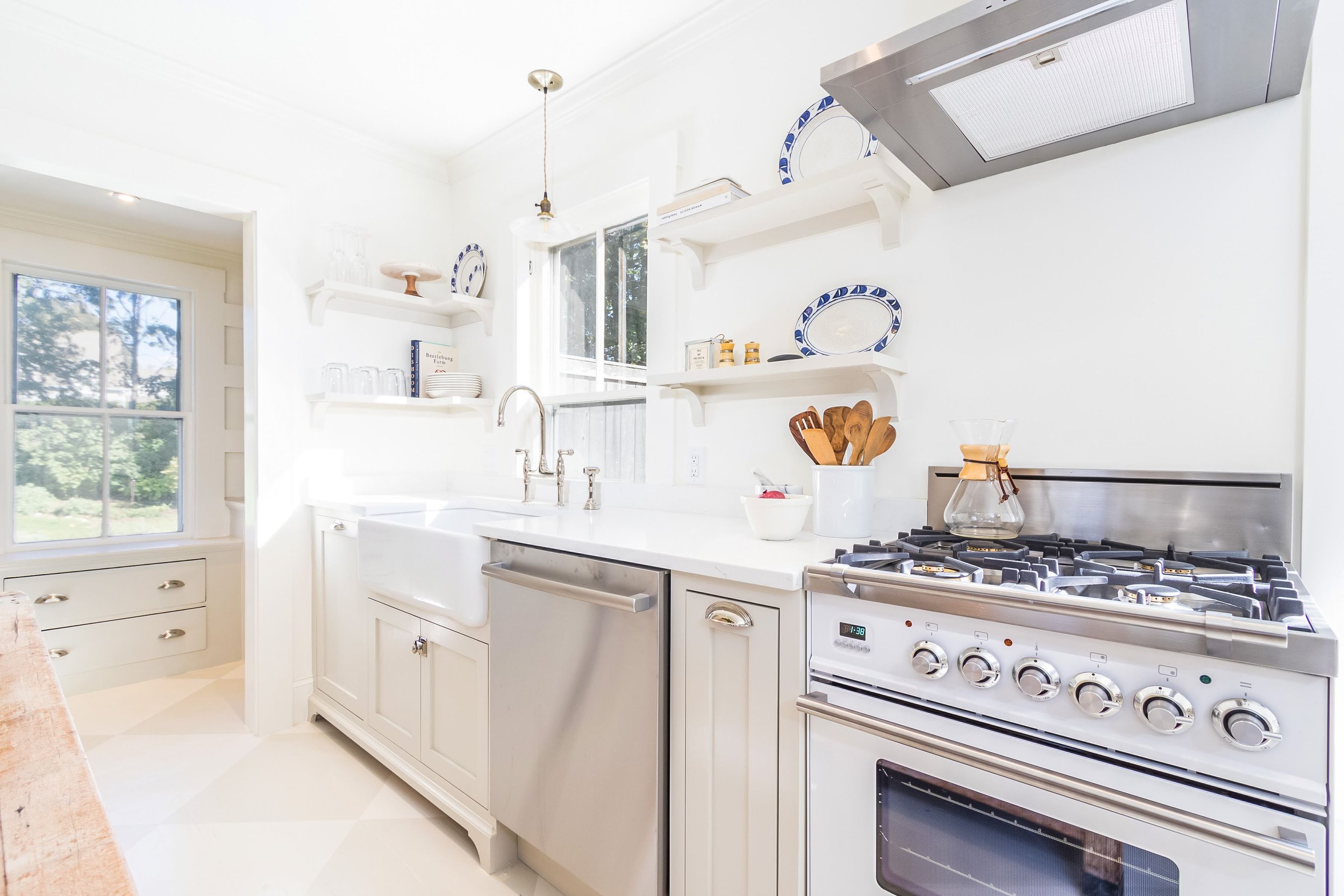 White custom coastal home kitchen with farmhouse sink, open shelves, stainless range, and bright Cape Cod details.