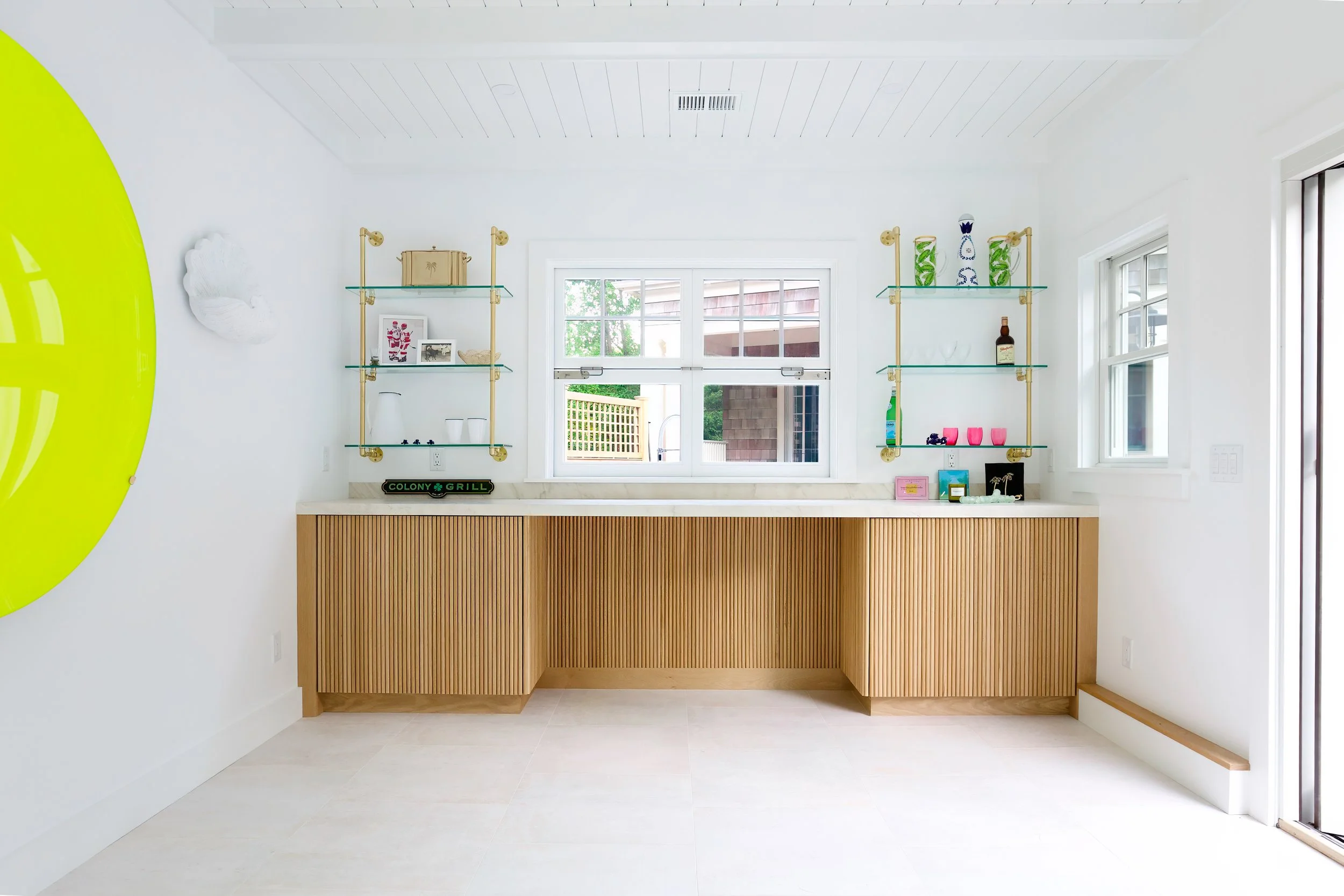 Pool house bar with wood-slat cabinetry, glass shelves, and bright entertaining space style.